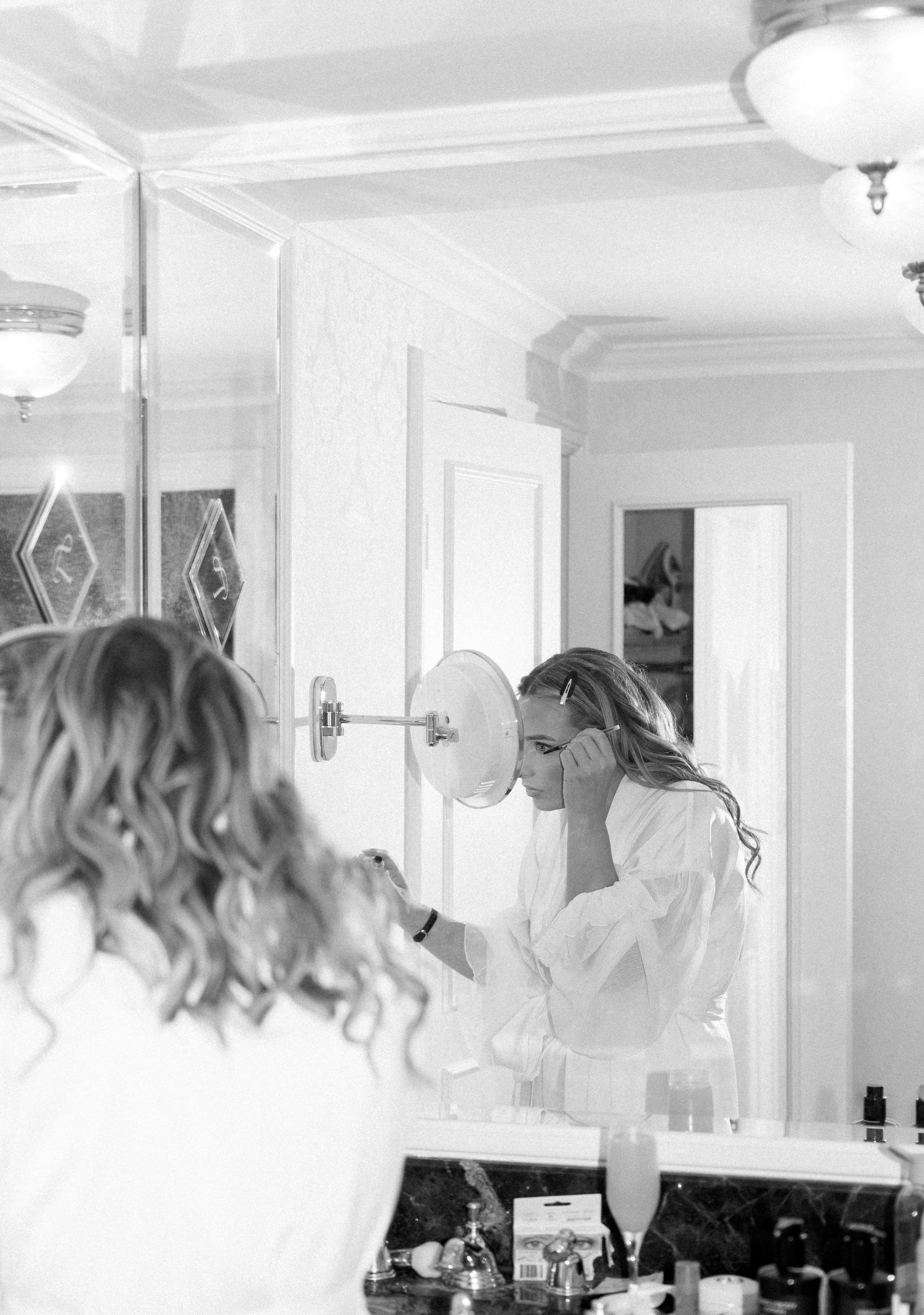 A black and white image showing a blurred reflection of hair in multiple bathroom mirrors.