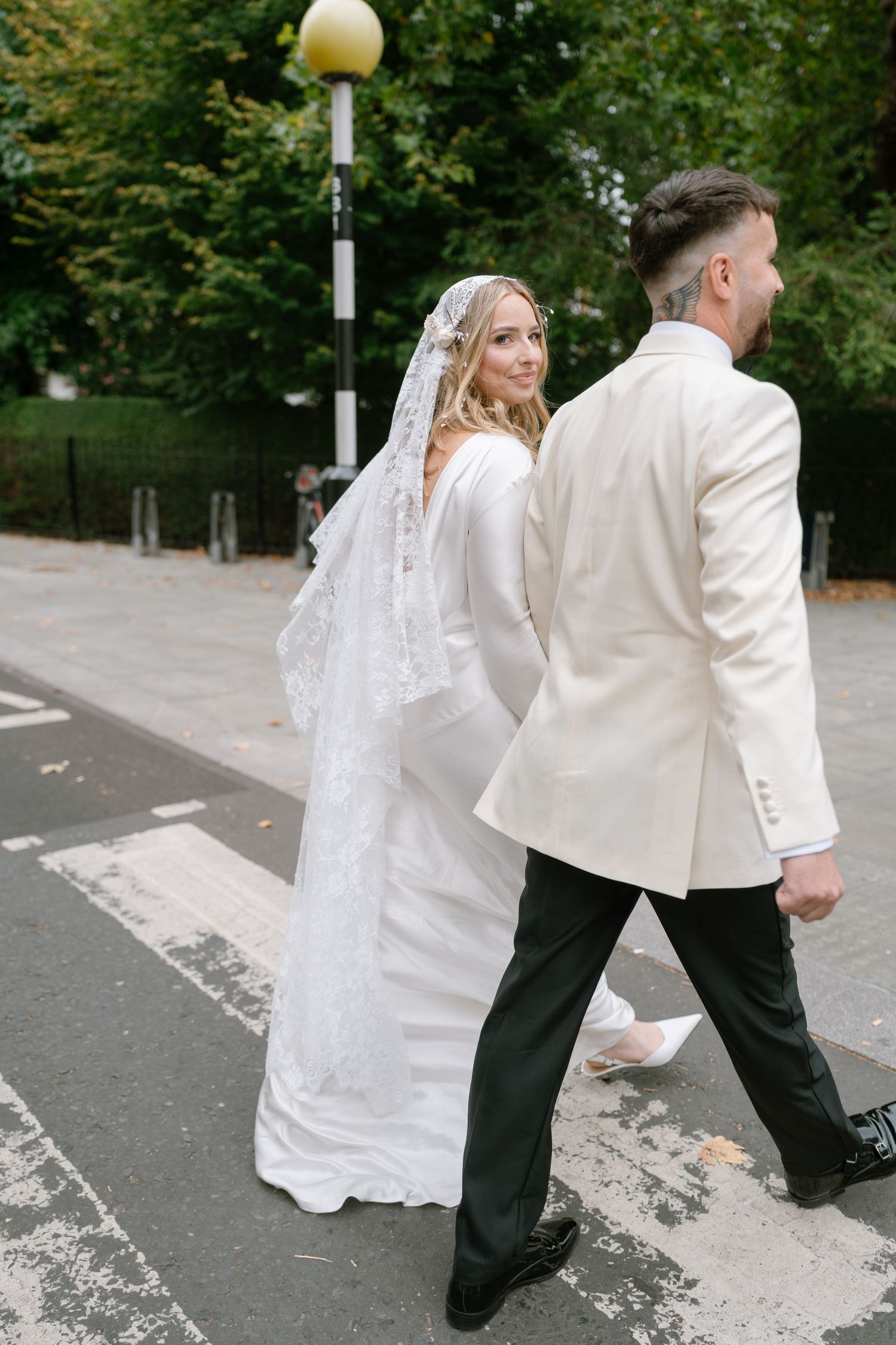 Newlyweds walking together outdoors in formal white wedding attire.