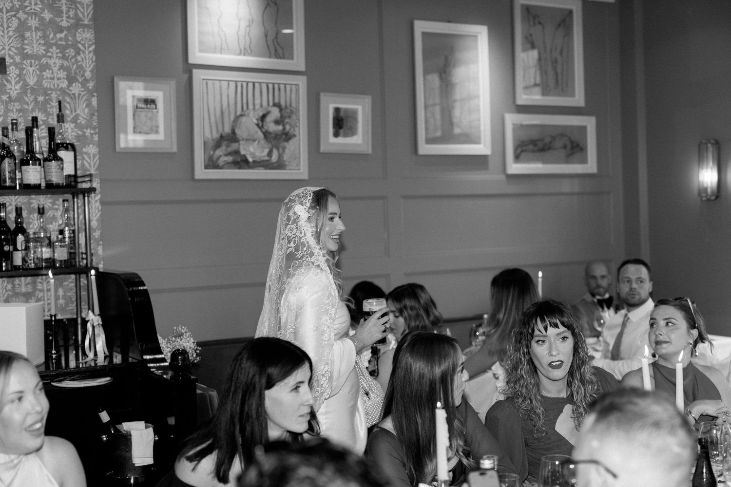 Wedding reception guests gather in a cozy bar area with framed artwork on the walls.