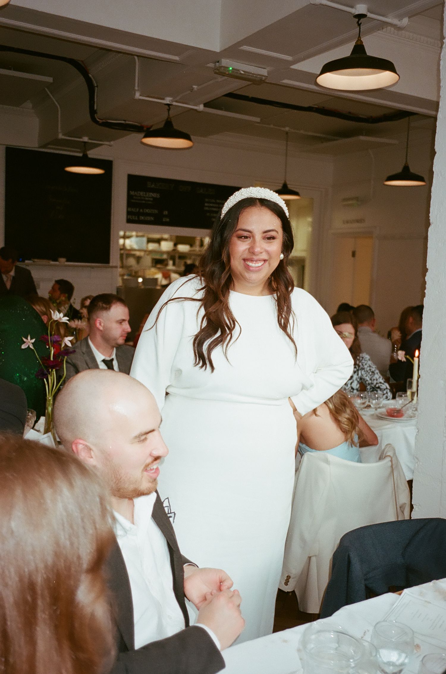 Wedding guests seated at tables in a bright indoor venue with industrial pendant lighting.