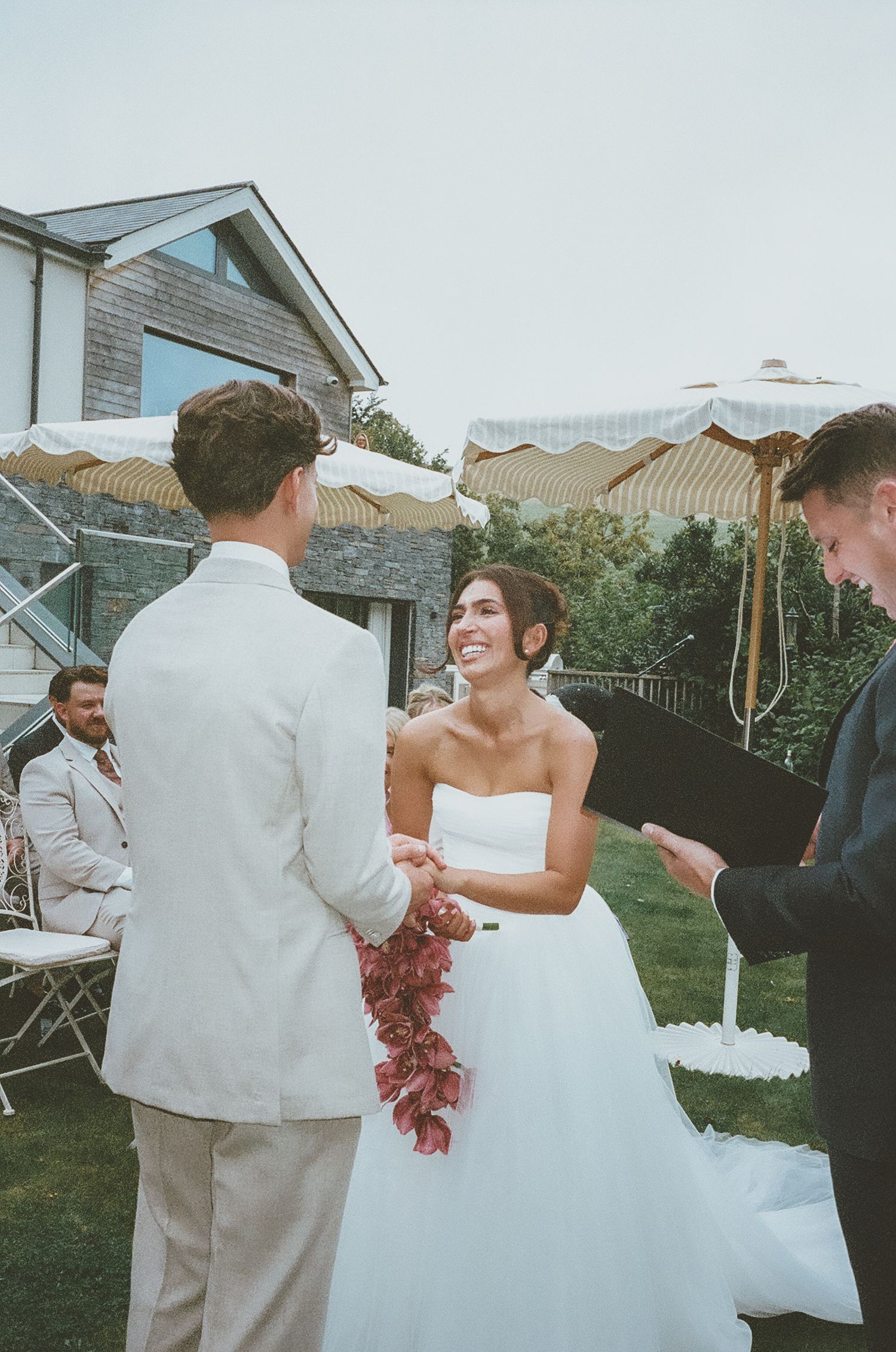 Wedding couple dances together at outdoor reception while guests watch and celebrate in backyard garden setting.