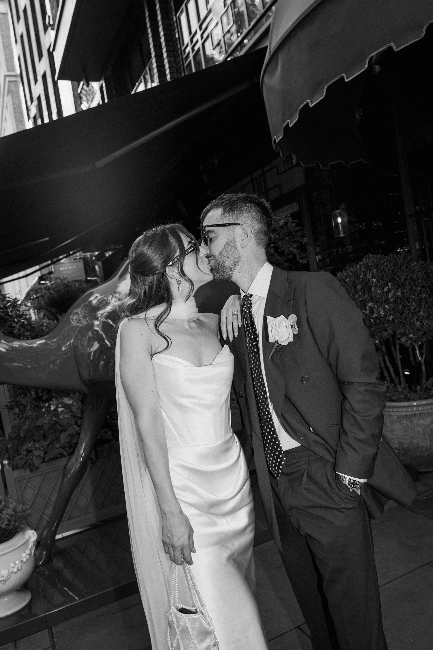 Black and white romantic portrait of bride and groom kissing outside urban restaurant venue.