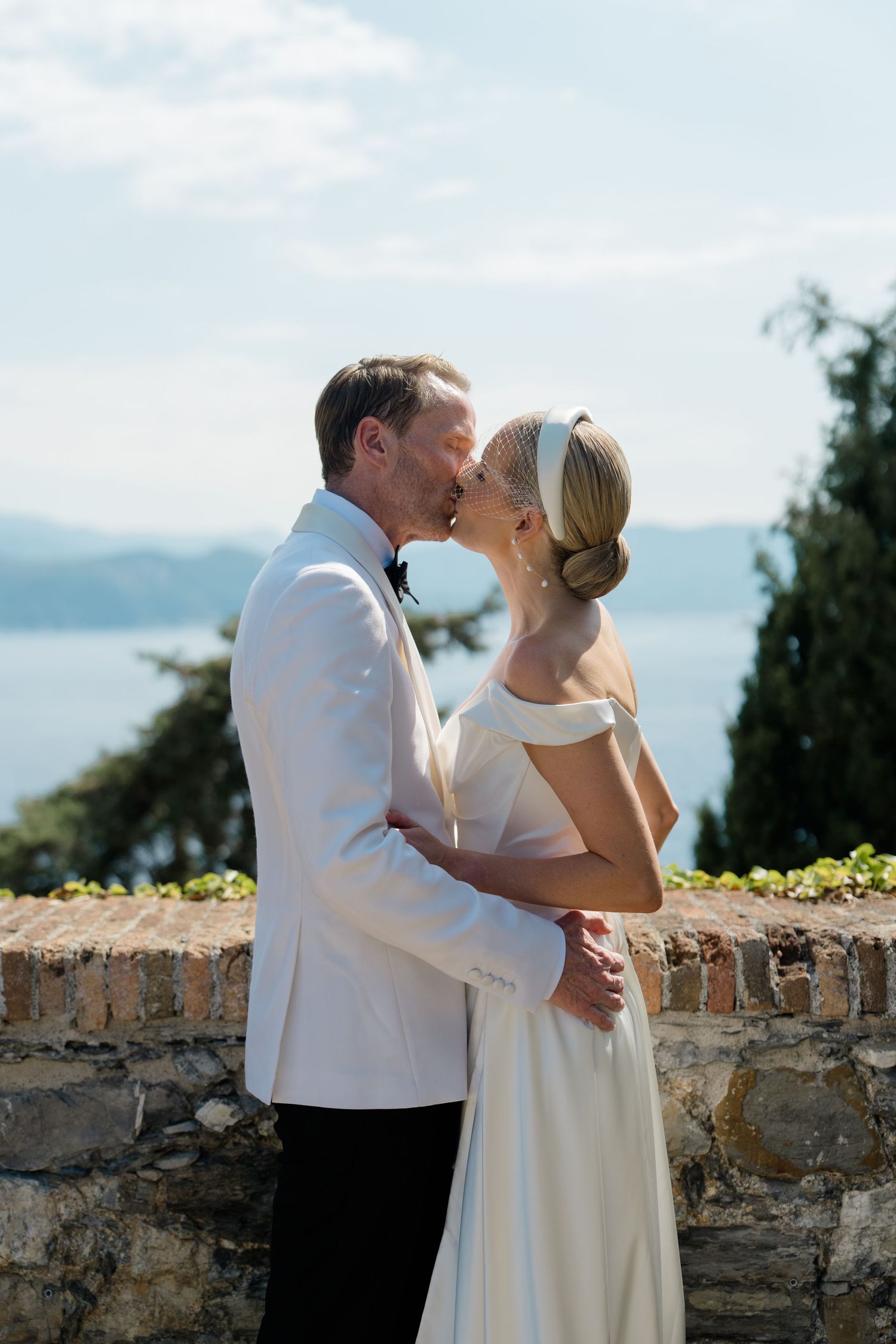 Bride and groom sharing a romantic kiss with scenic lake and mountains backdrop.