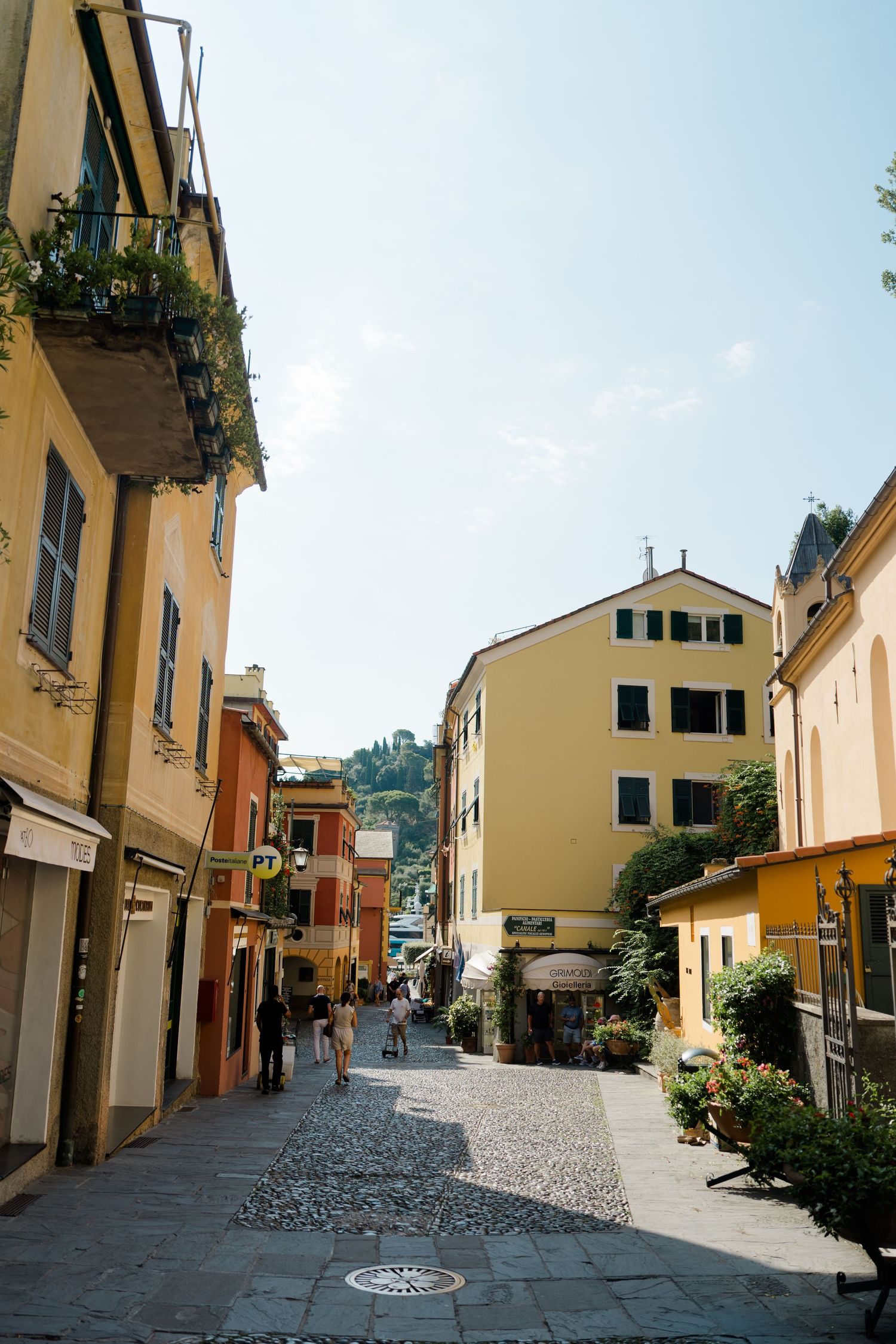 Sunny cobblestone street lined with colorful yellow and orange buildings in a charming Italian coastal village.