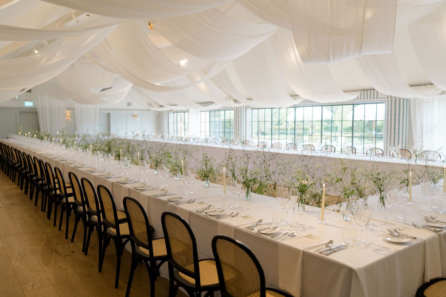 Elegant wedding reception hall with long tables, white draping ceiling and floral centerpieces.