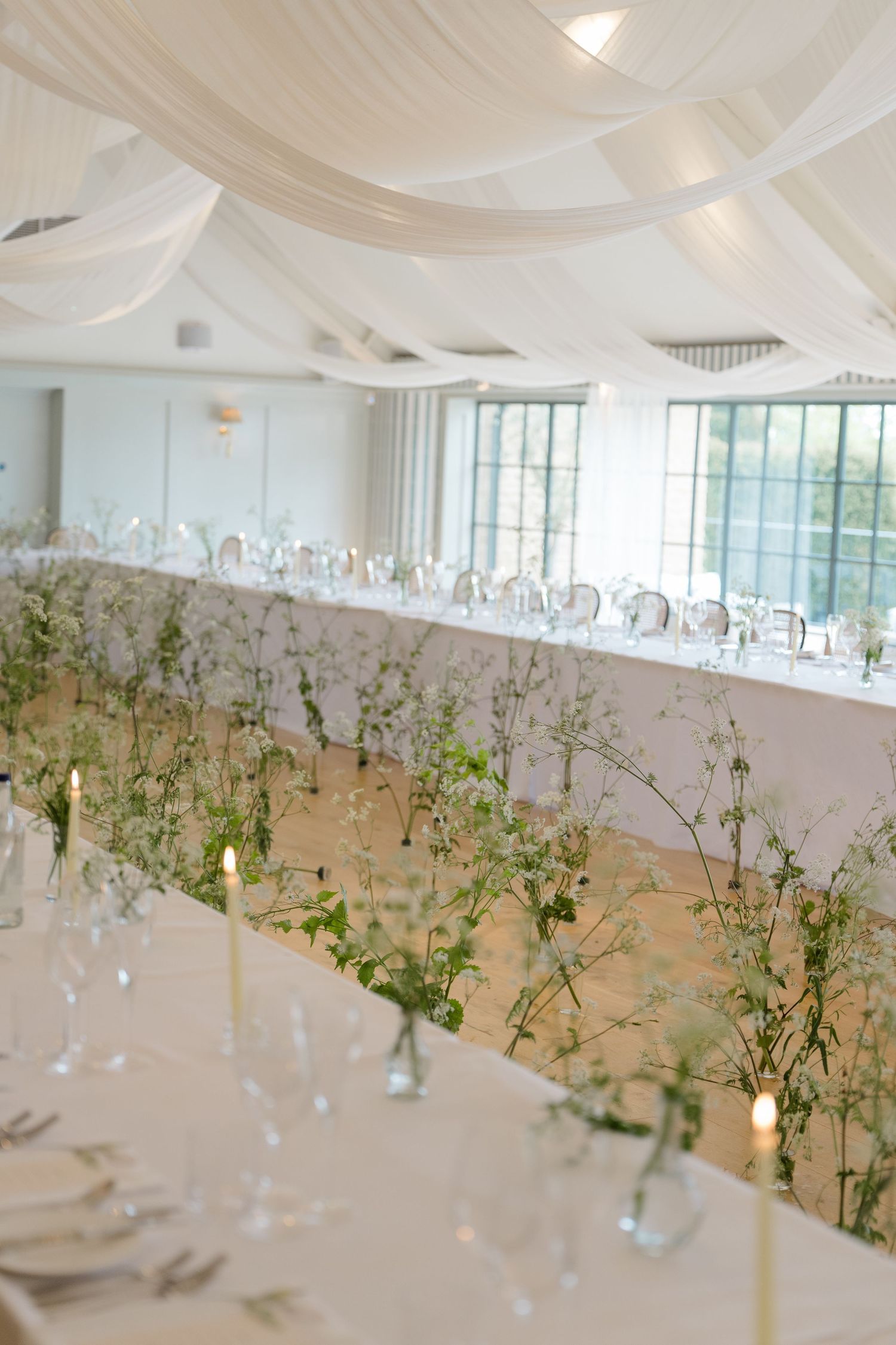Stunning wedding reception hall with white draped ceiling, long tables adorned with greenery and candles.