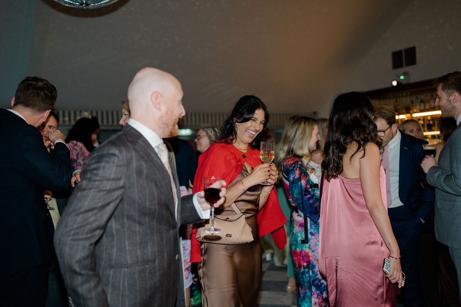 Wedding guests mingle and toast with drinks at colorful evening reception.