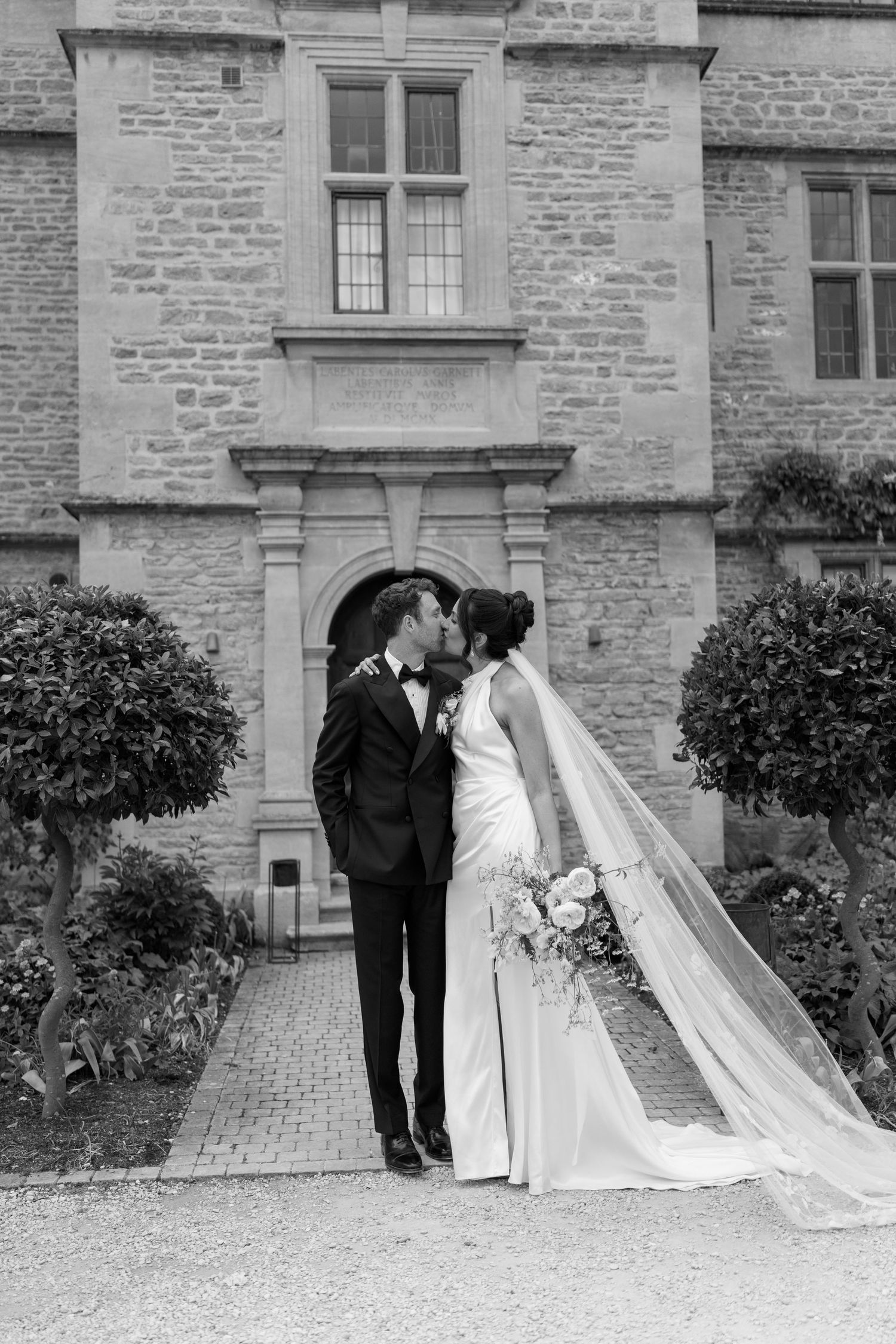 Bride and groom share romantic kiss outside historic stone manor on wedding day.