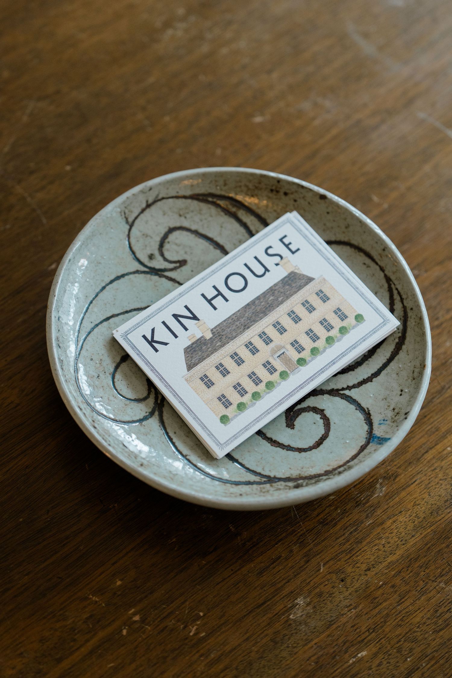 Kin House business card resting in a decorative ceramic bowl on wooden table.