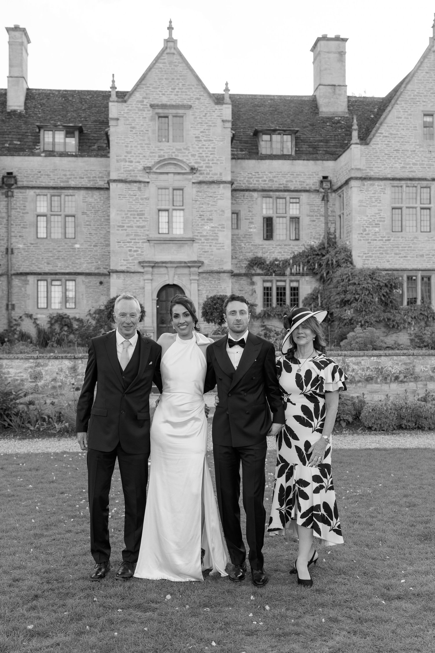Bride and groom pose with family members outside a grand stone manor house on wedding day.
