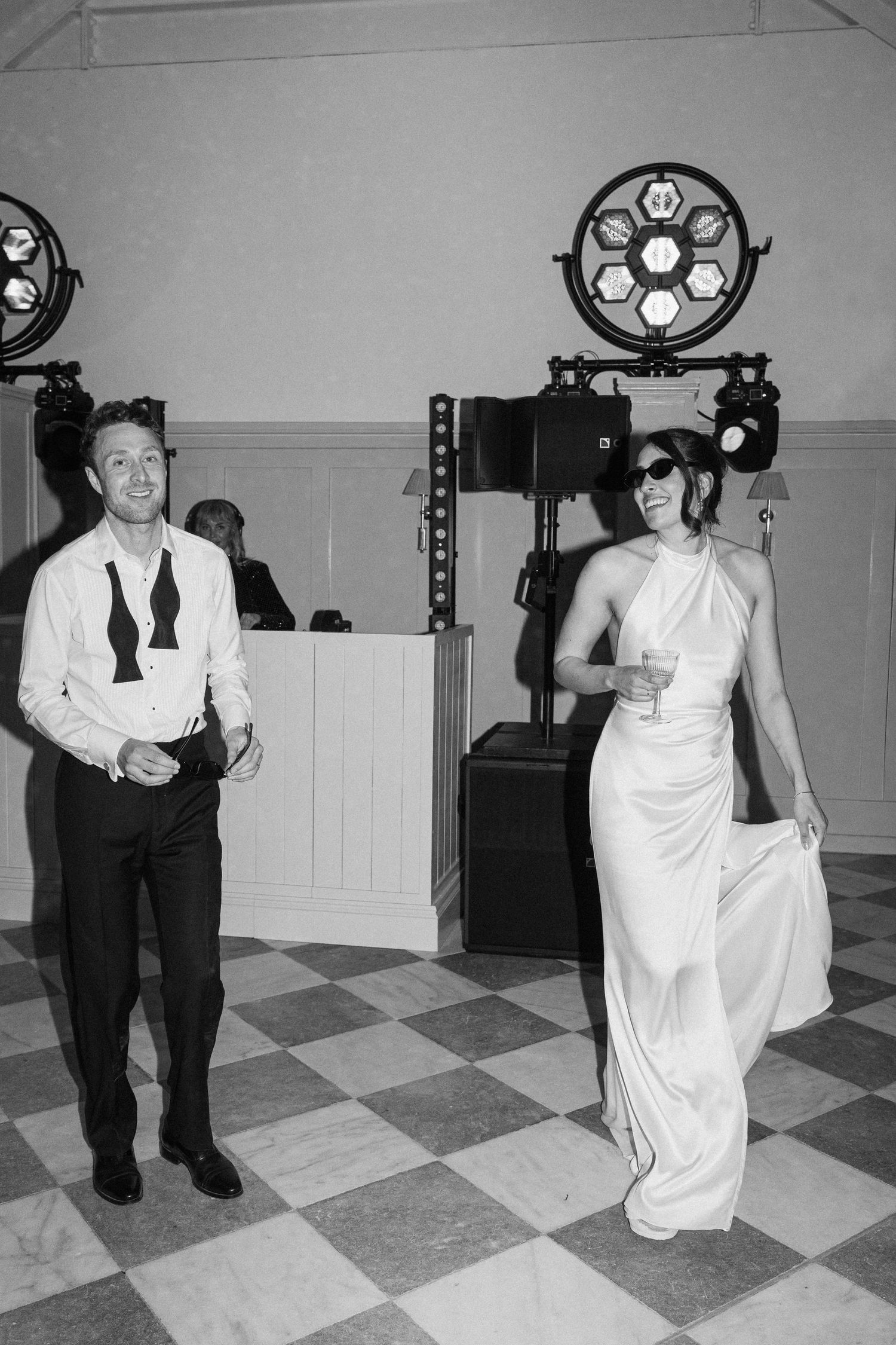 Black and white photo of bride in halterneck gown wearing sunglasses dancing with groom at wedding reception.