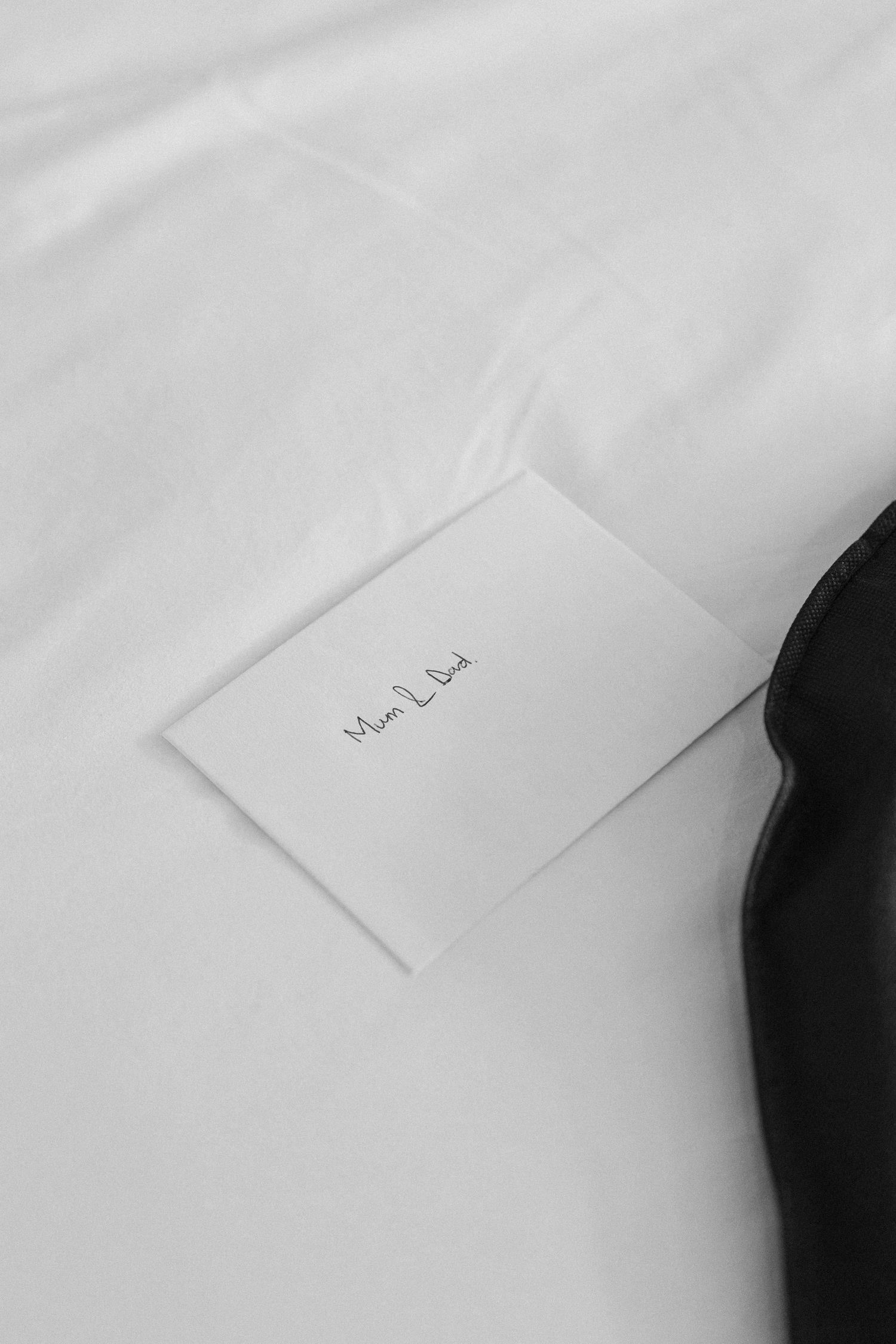 Minimalist black and white photo of a small handwritten note card on white bed linens.