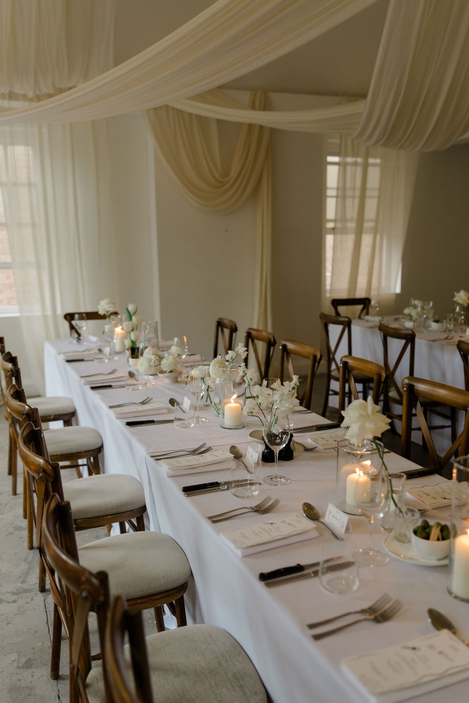 Elegant wedding reception room with long white-draped tables, candles, and floral centerpieces.