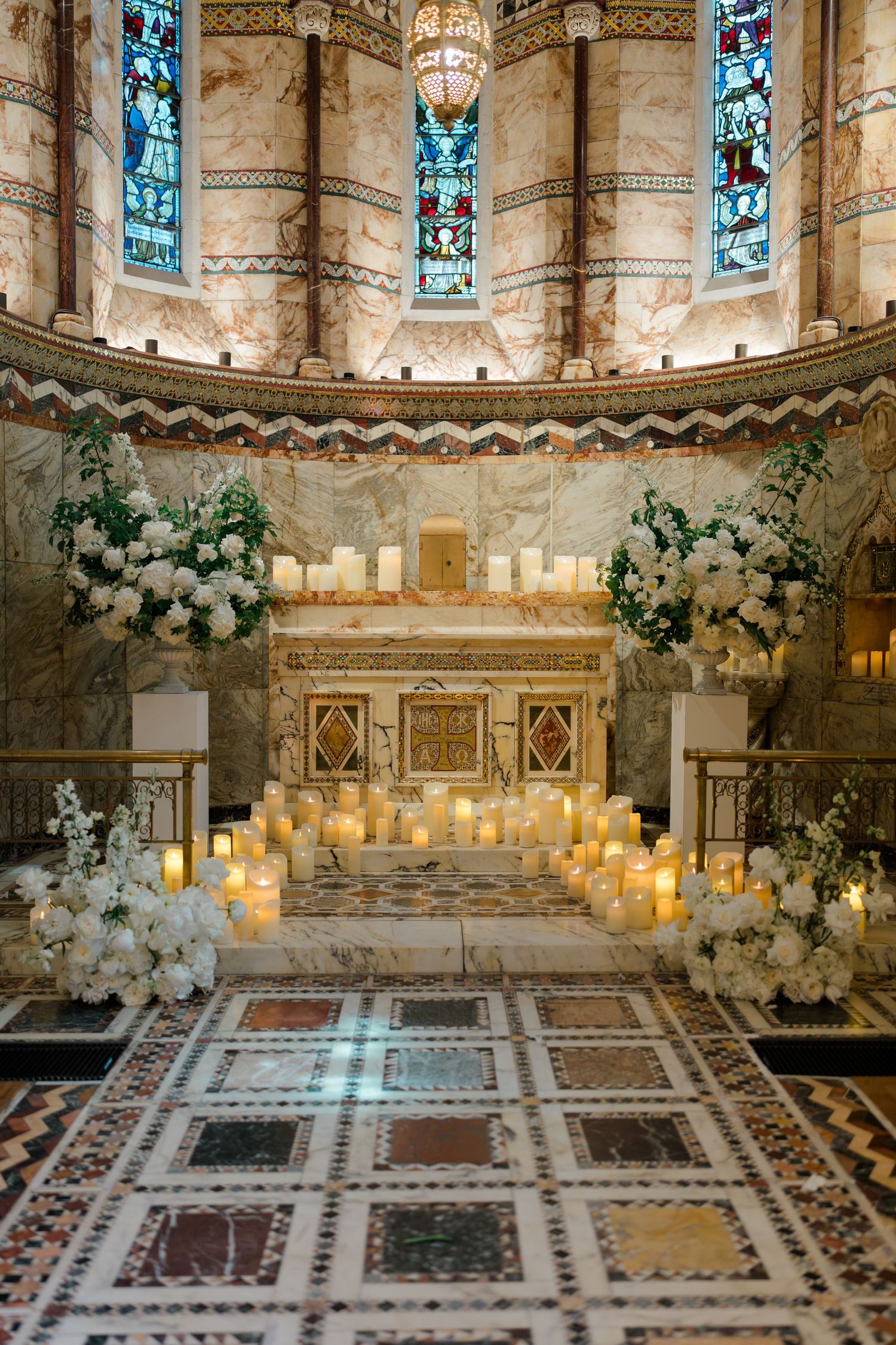 Ornate church altar adorned with white floral arrangements and glowing pillar candles for wedding.