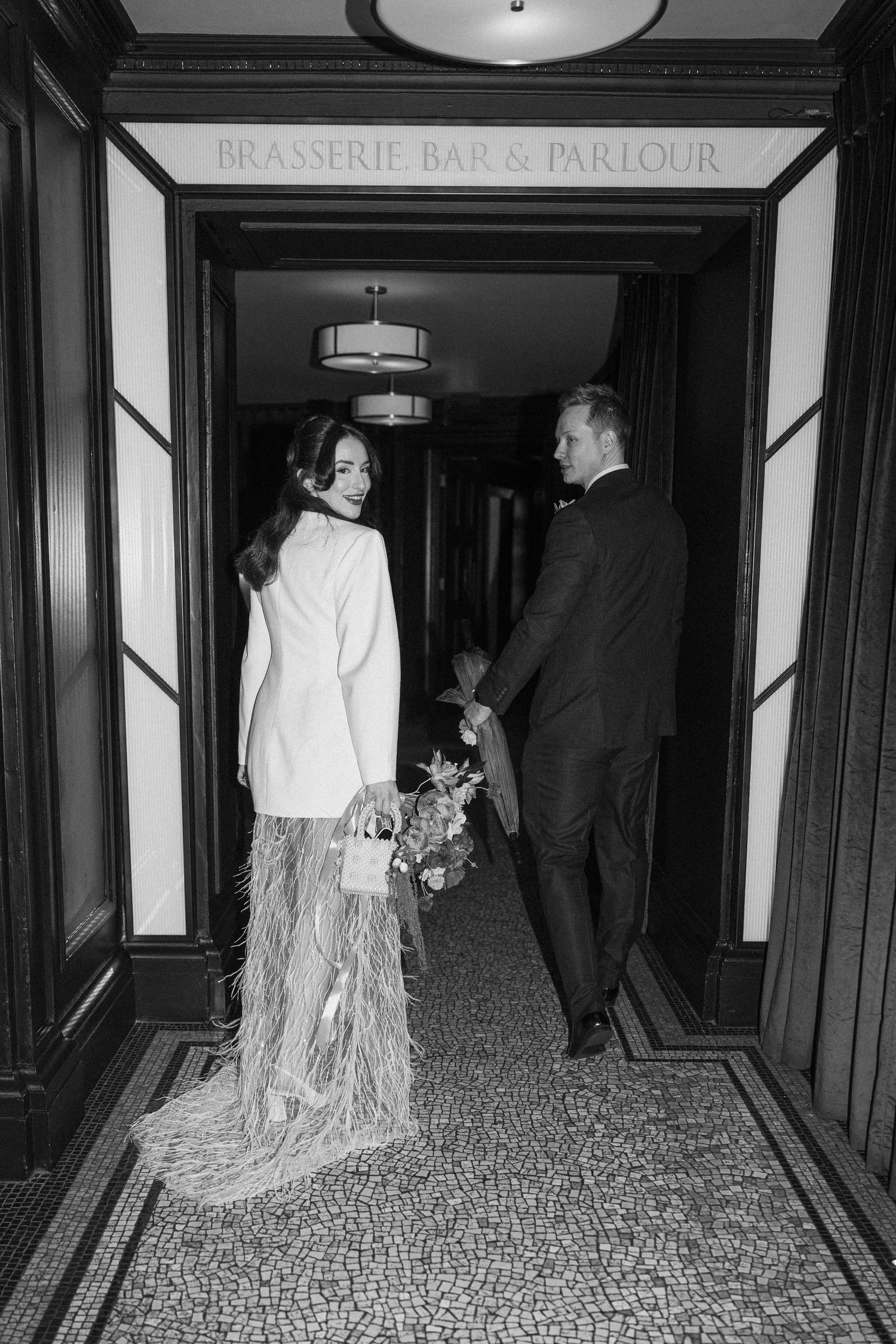 Bride in white feather skirt and groom entering Brasserie Bar and Parlour.