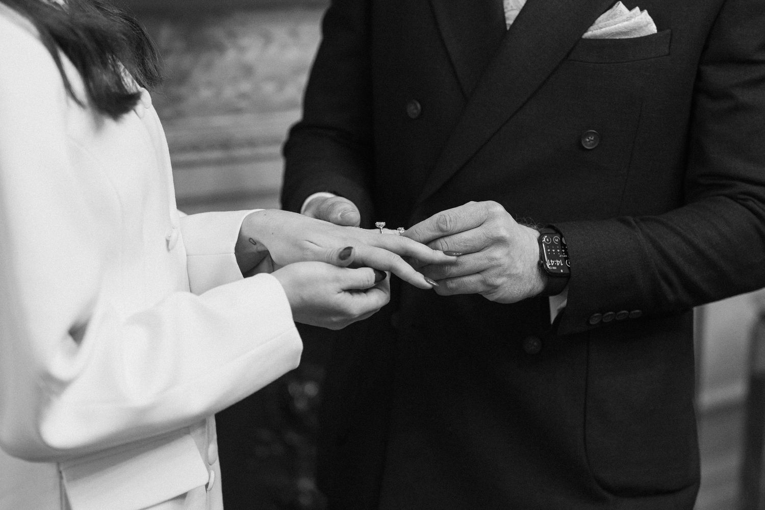 Black and white close-up of bride and groom exchanging wedding rings during intimate civil ceremony.