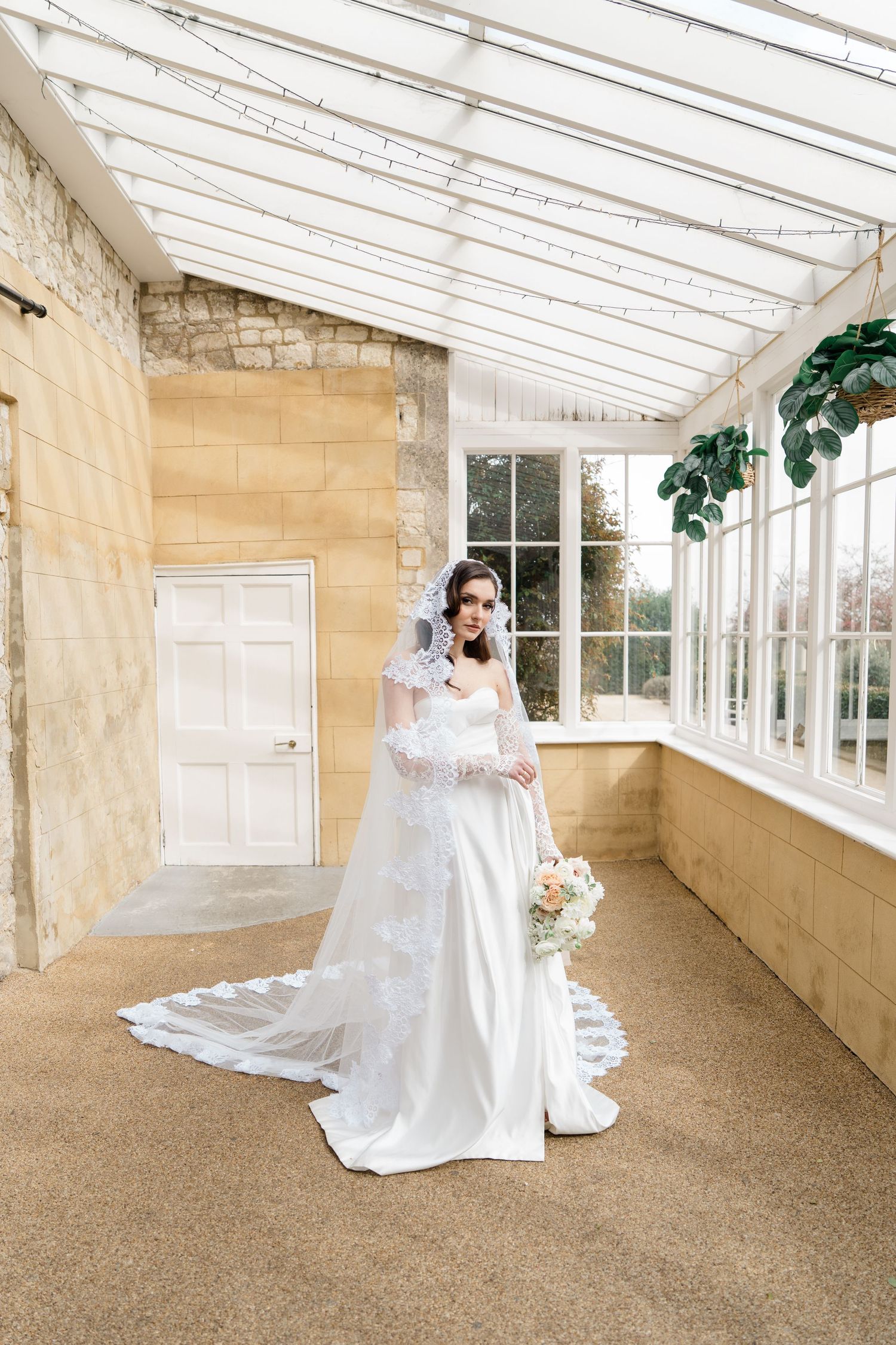 Wedding portraits in a sunlit conservatory with glass ceiling and stone walls.