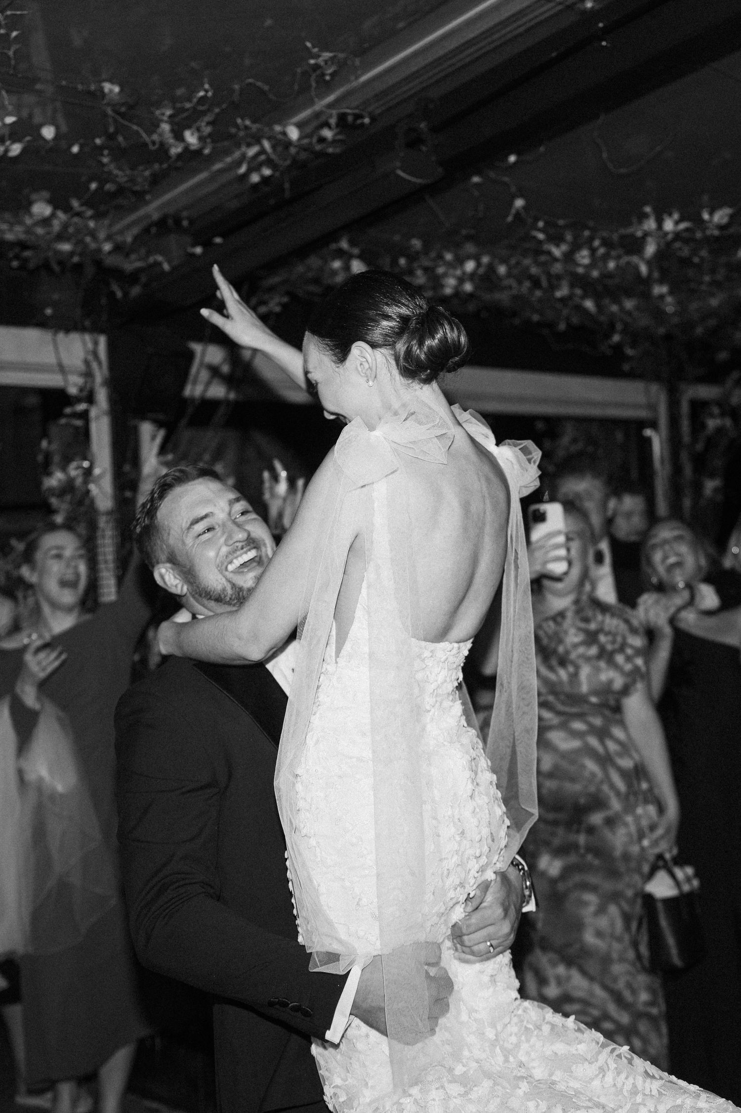 A couple embraces while dancing at their wedding reception as guests look on.