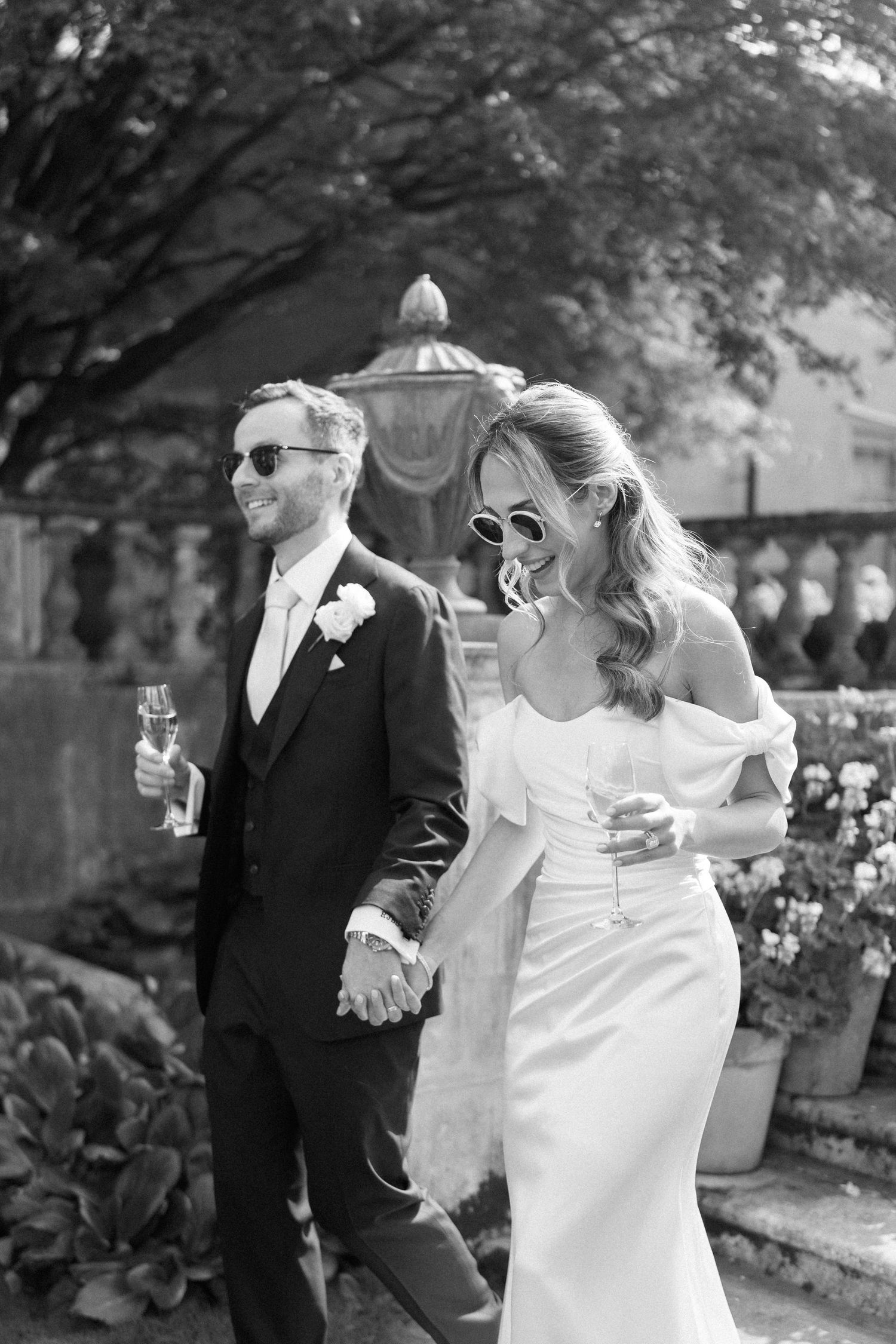 Black and white photo of a couple sharing champagne in a garden setting.