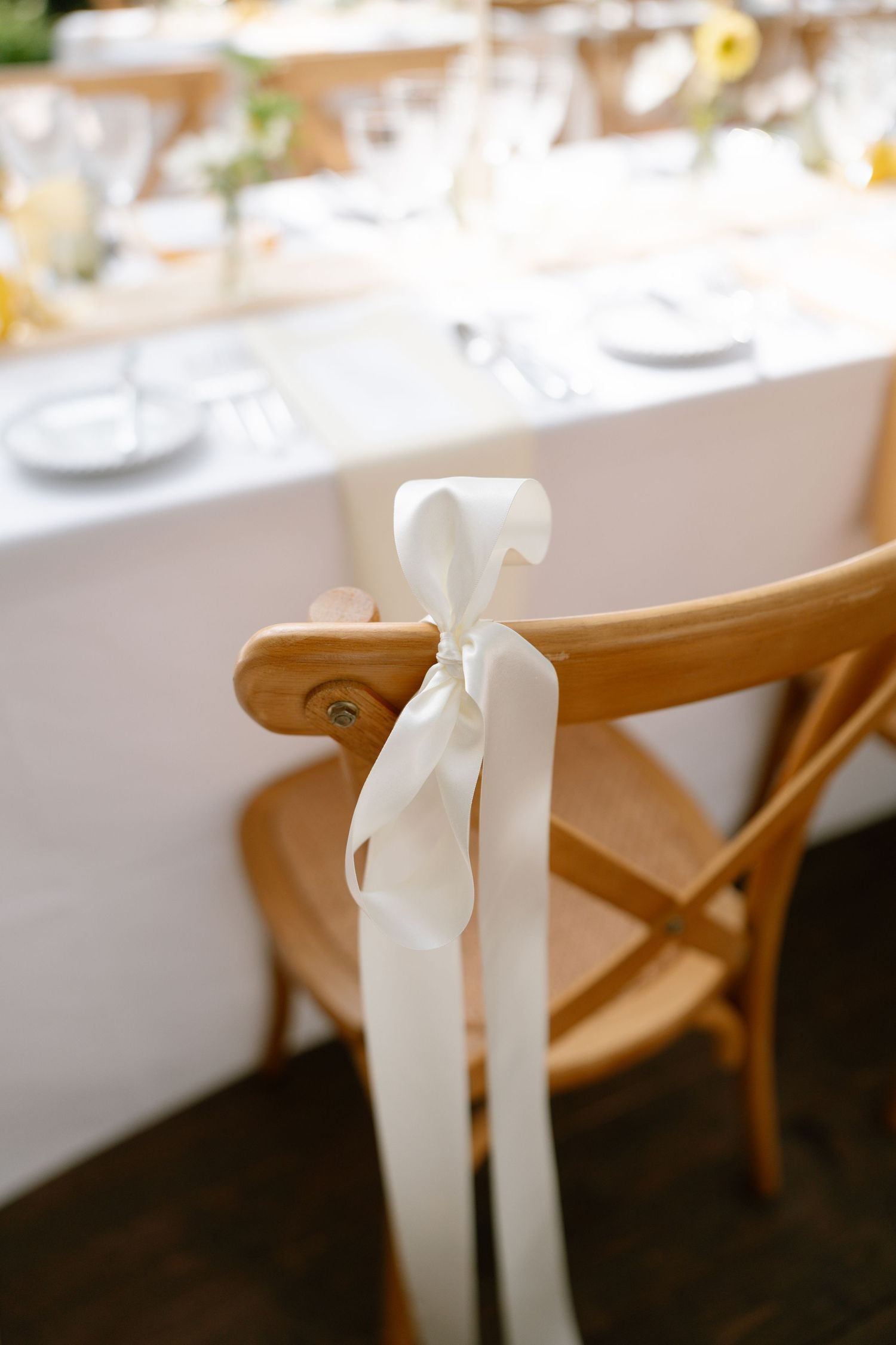 White ribbons tied to wooden chairs at an elegant wedding reception.
