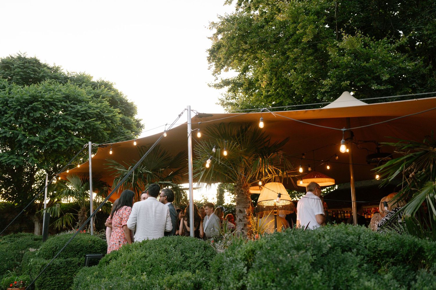 Outdoor wedding reception tent illuminated at dusk with string lights.