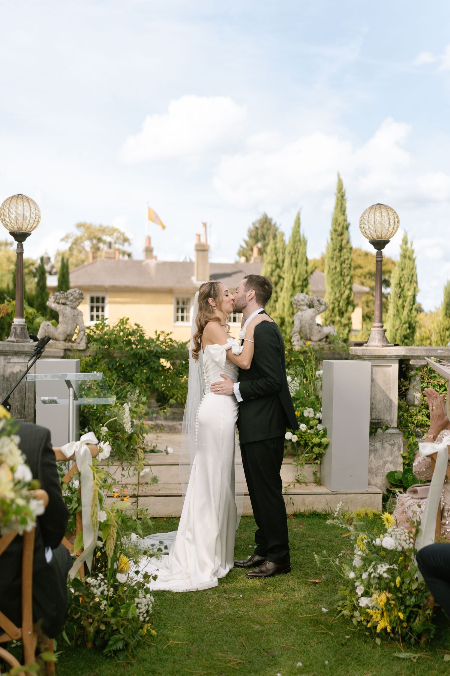 Elegant garden wedding ceremony with couple kissing among floral arrangements and decorative lanterns.