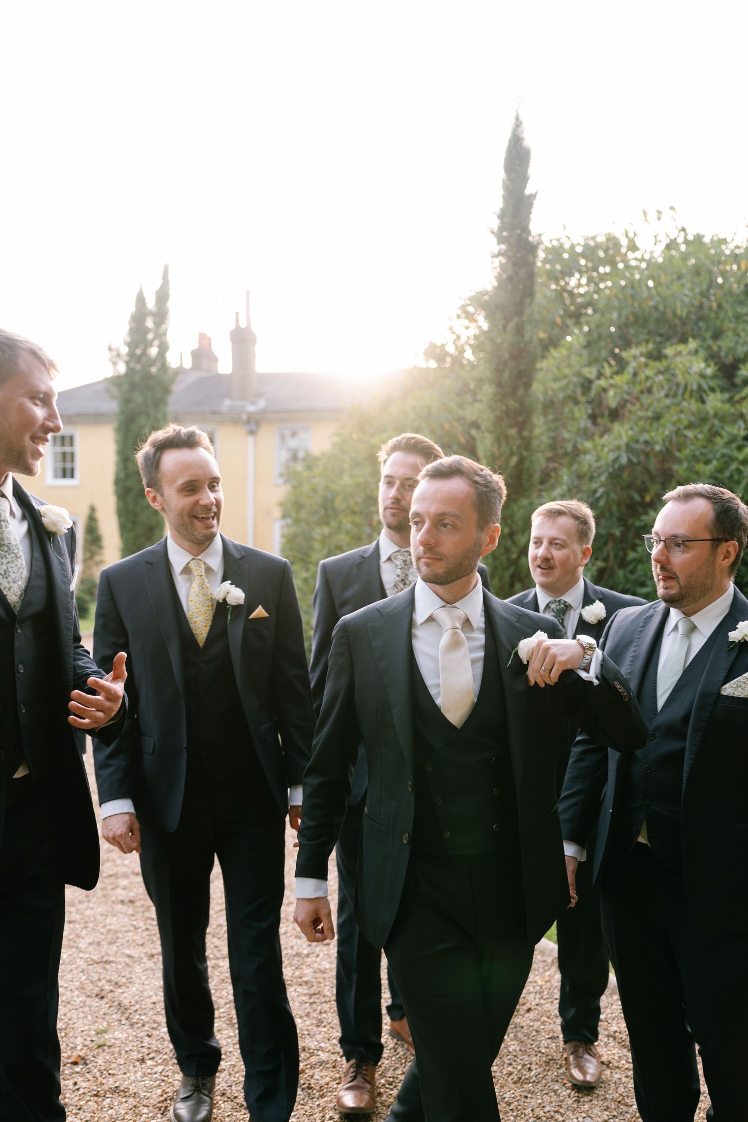 Groomsmen sharing a candid moment while walking together at sunset outside a classic building.