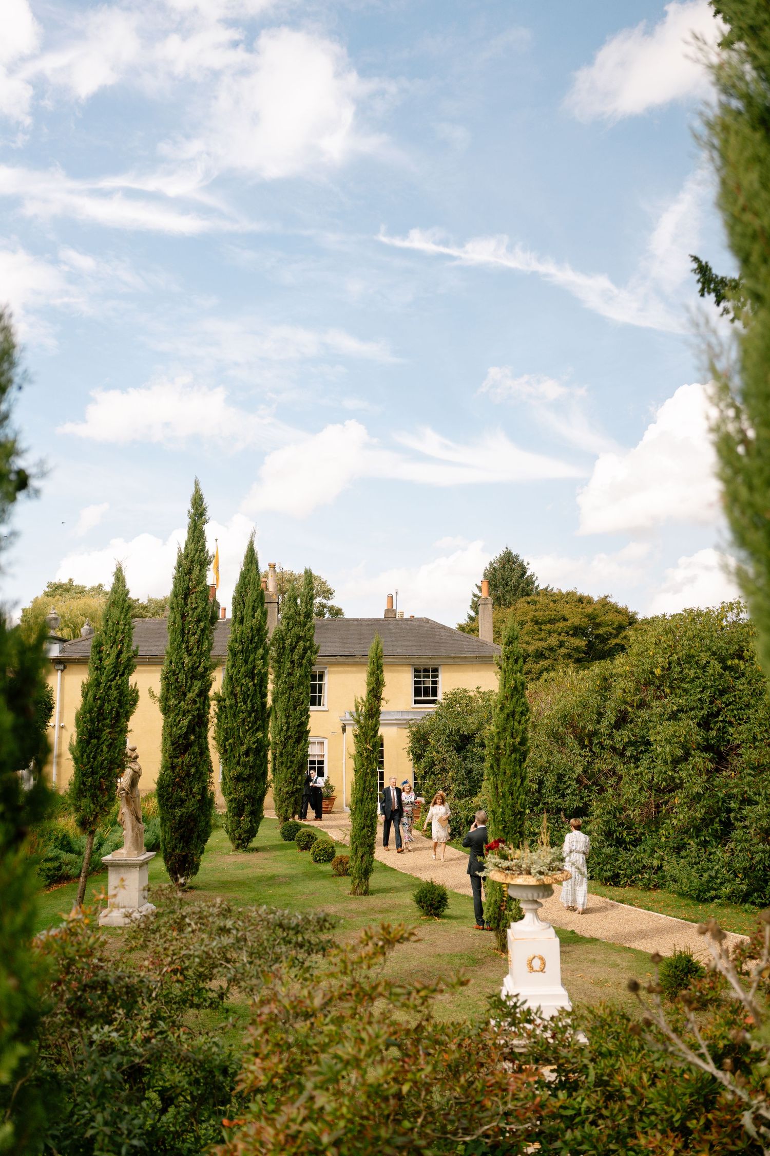Elegant country estate with manicured gardens and cypress trees under blue skies.