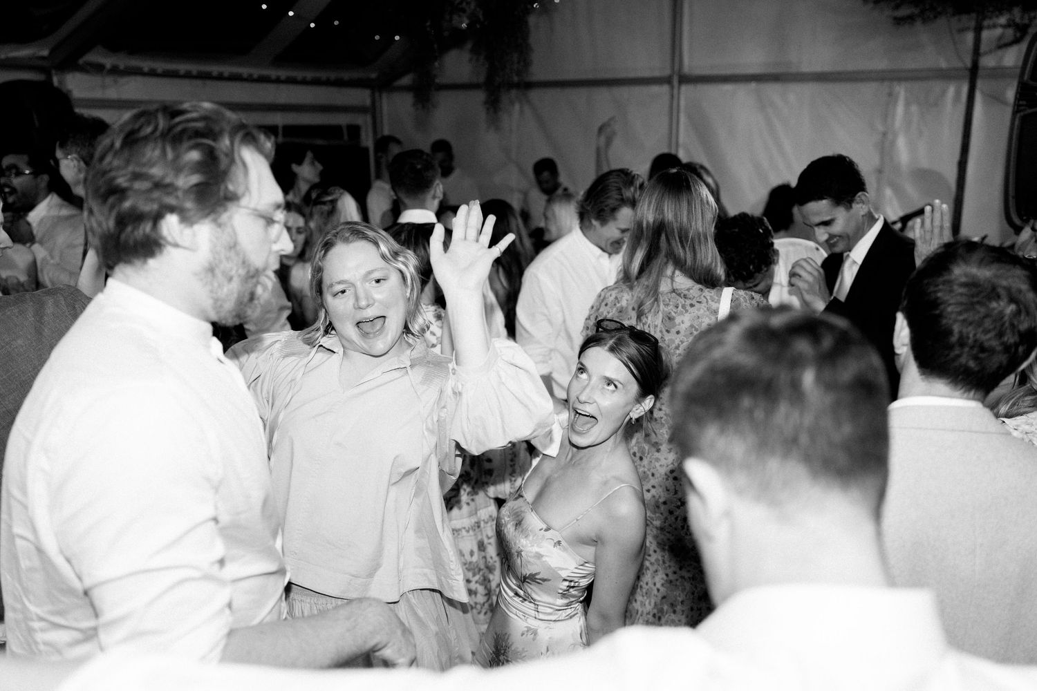 Lively wedding reception dance party scene with guests celebrating under a tent.