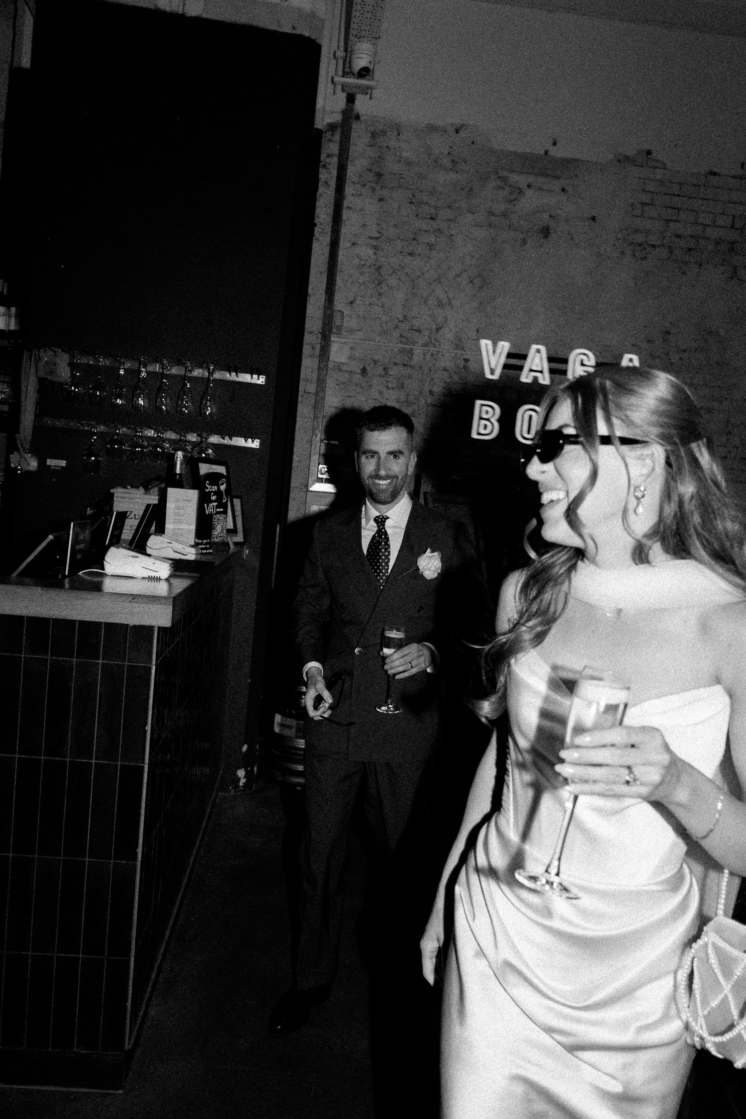 Black and white candid photo of bride in satin gown laughing at evening wedding reception.