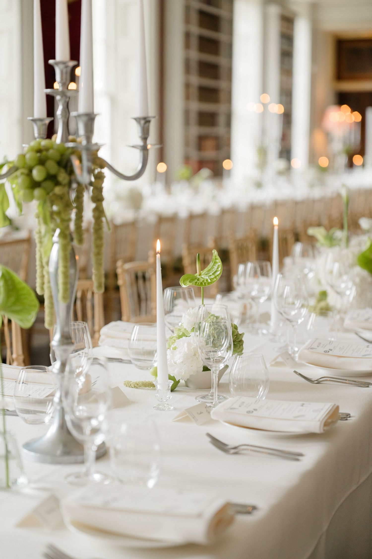 Elegant wedding reception table set with white linens, candles, and green floral centerpieces.