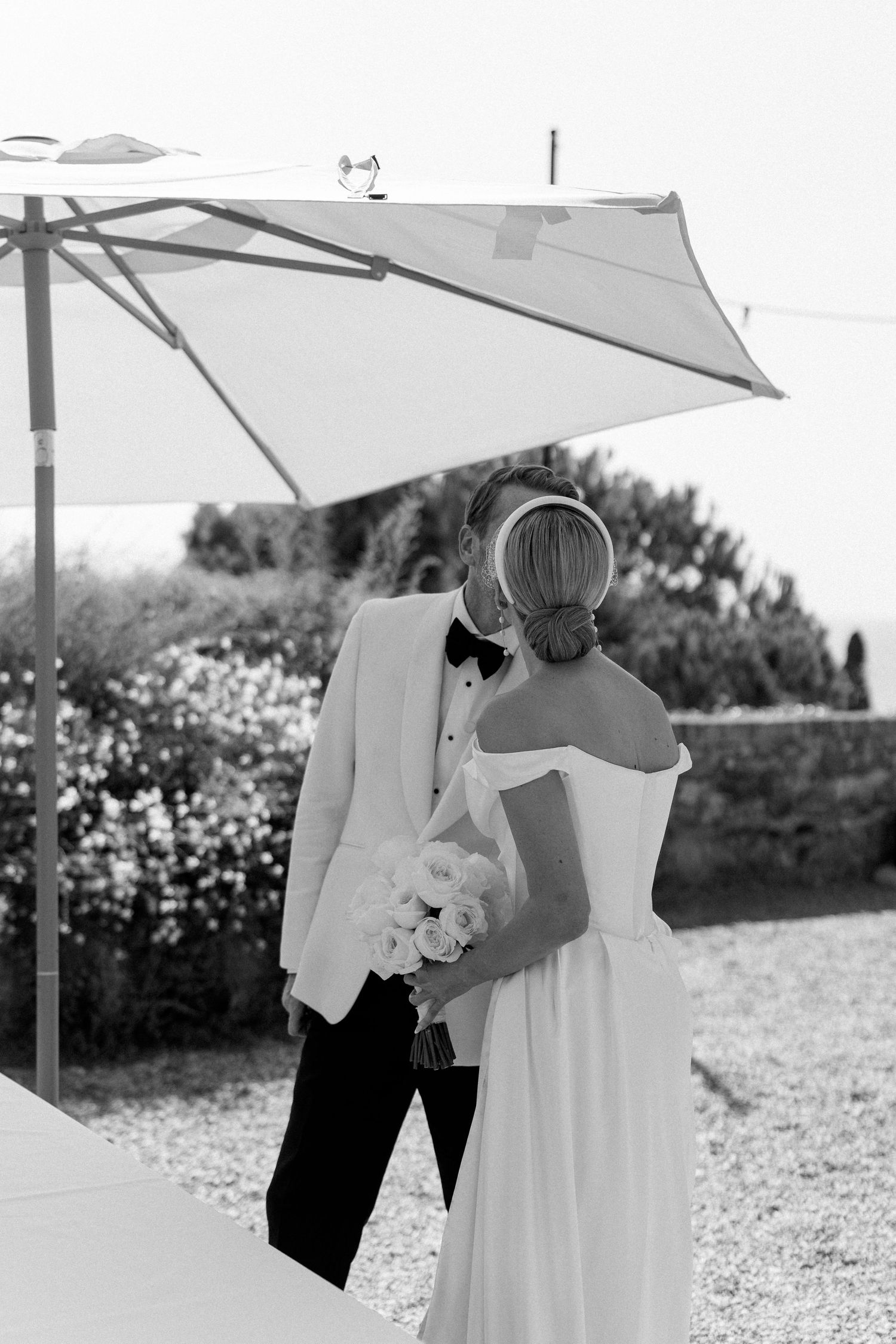 Bride and groom sharing intimate moment under white umbrella outdoors in black and white wedding photo.
