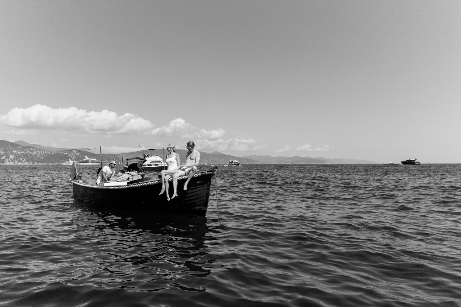 Black and white photo of small wooden boat with wedding party floating on calm open sea.