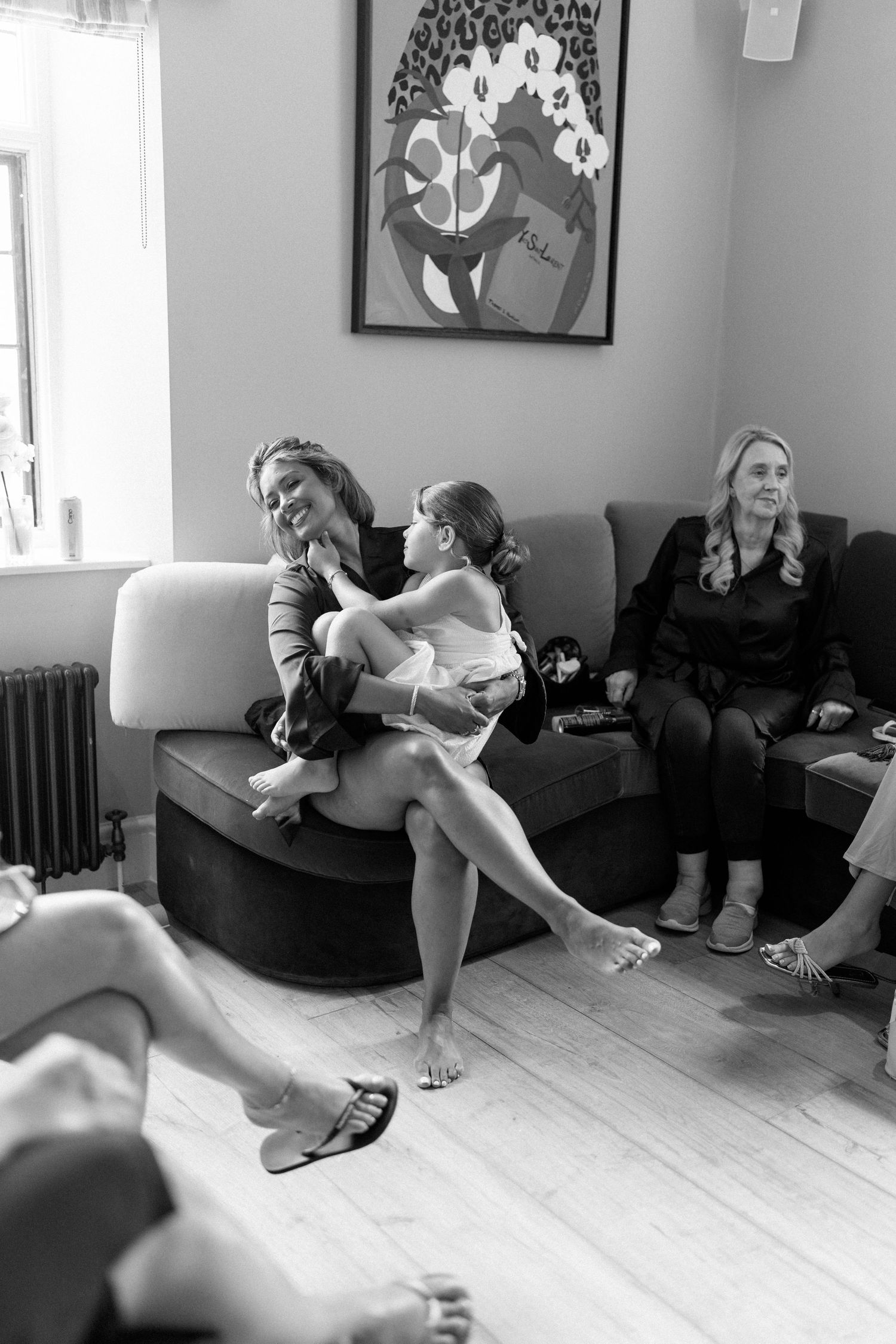 Black and white photo of women relaxing on a sofa with a child during wedding preparations.