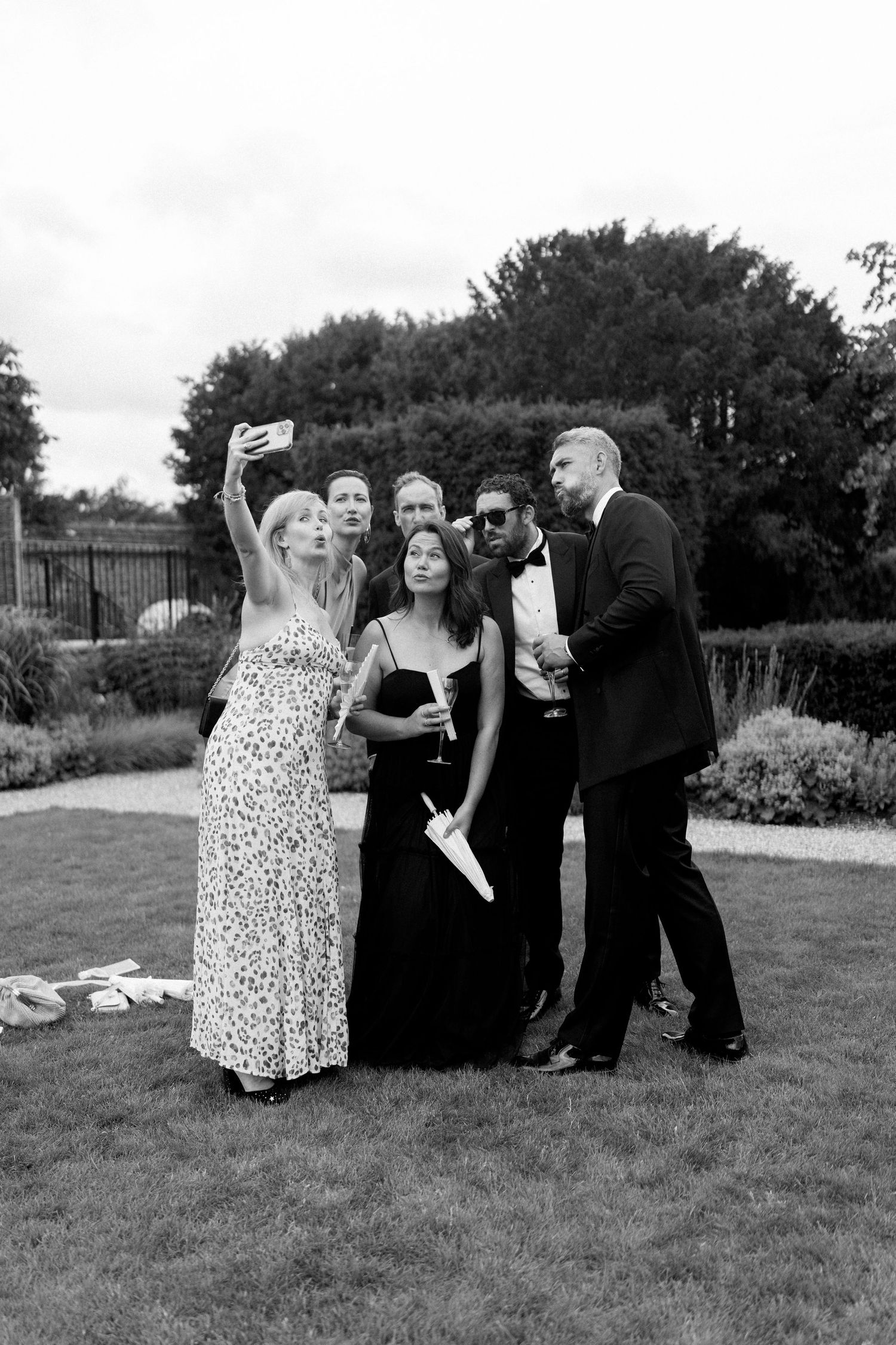 Wedding guests take a group selfie on the lawn at an elegant outdoor reception.