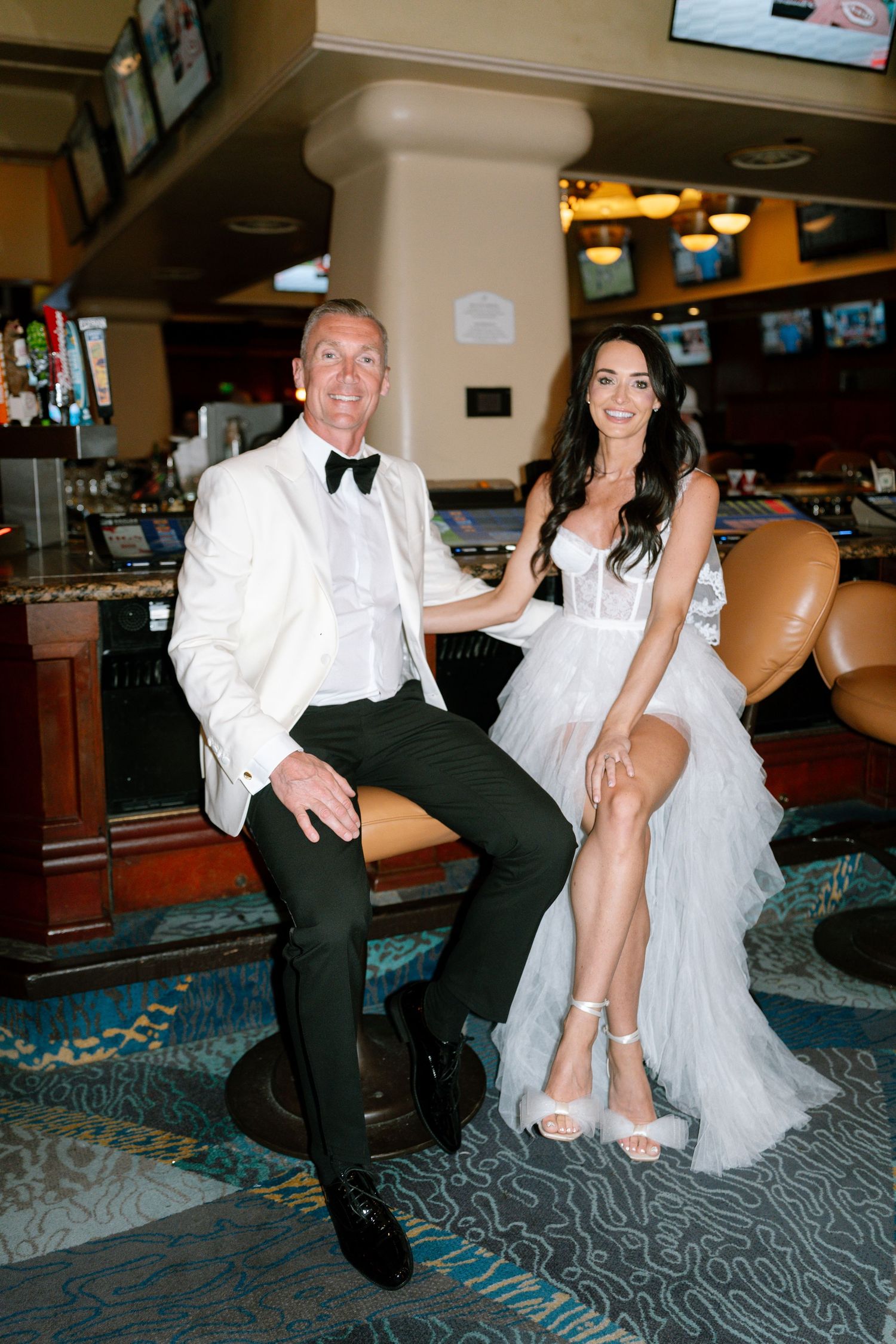 Newlyweds in formal attire pose playfully at a bowling alley with white dress and tuxedo.