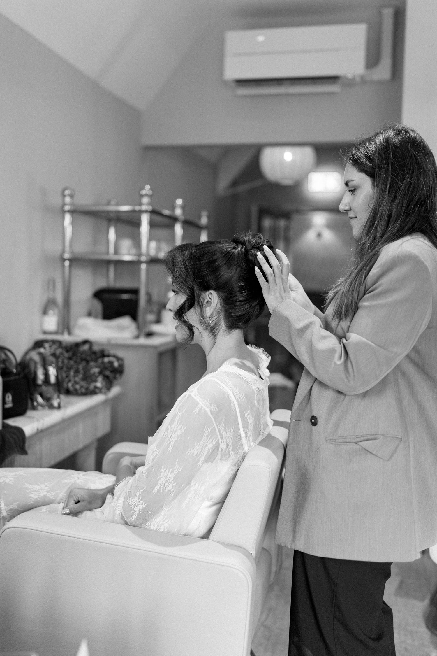 Black and white photo of hairstylist styling brides updo in a wedding preparation salon.
