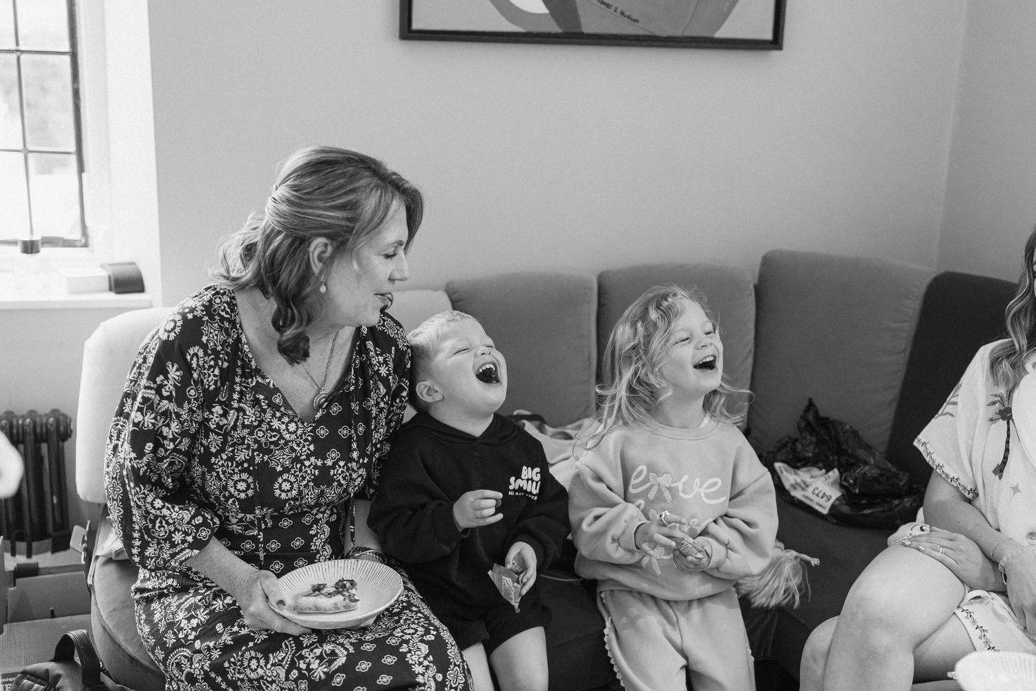 Black and white photo of a woman and two laughing children sitting together on a sofa.