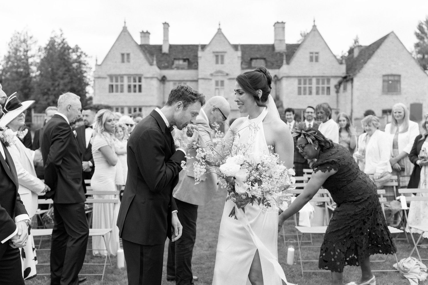 Newlyweds walking through confetti shower outside elegant English manor house after ceremony.