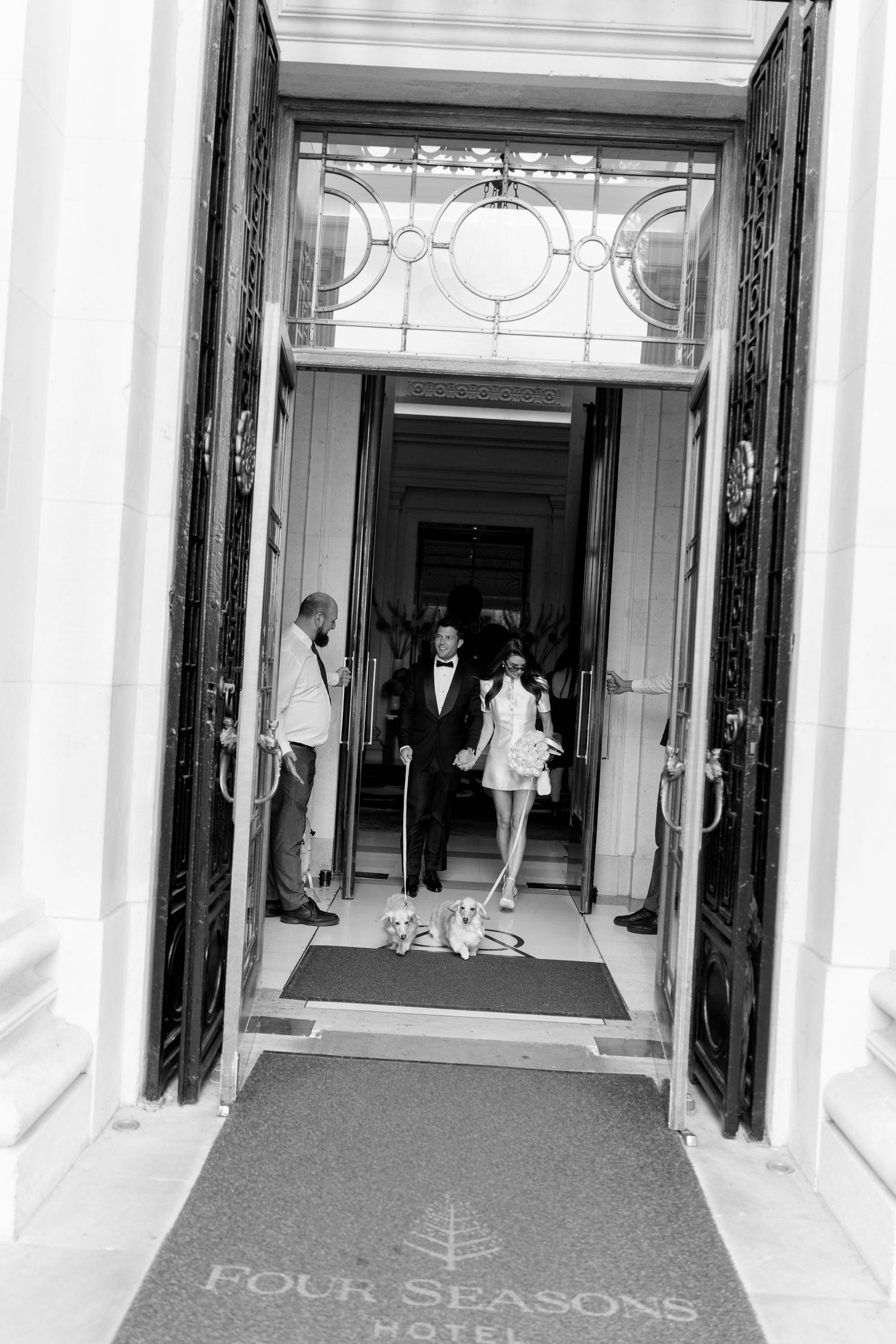 Black and white photo of newlyweds exiting Four Seasons Hotel with two small dogs on wedding day.