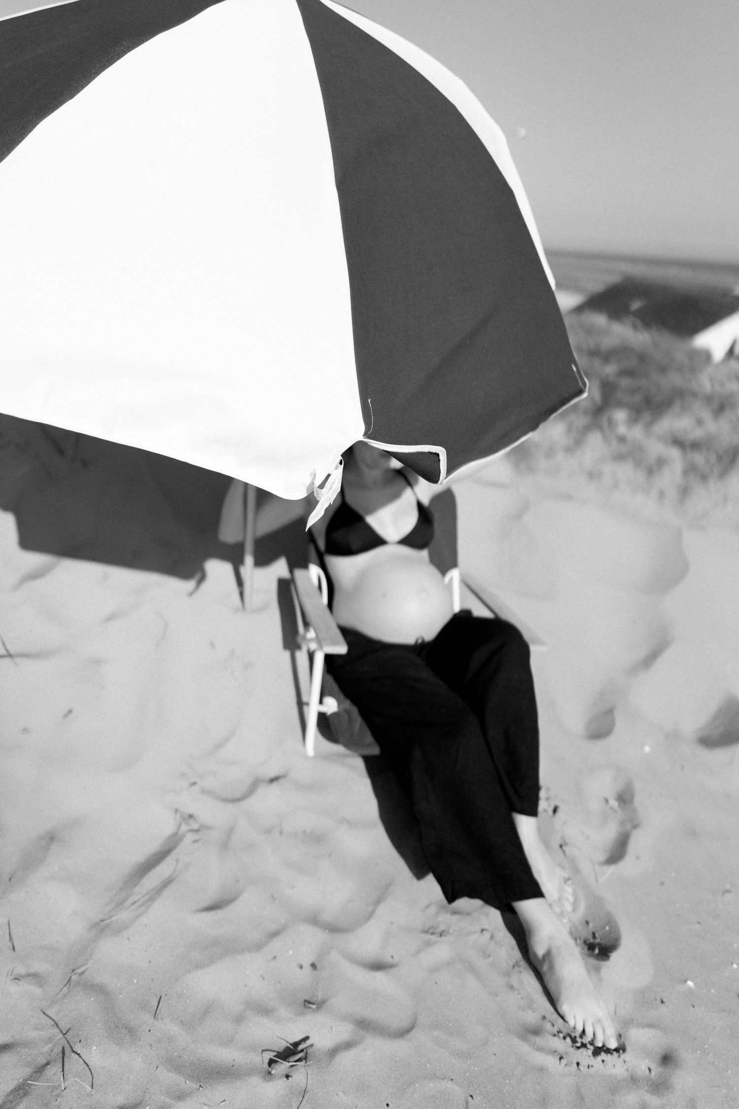 Black and white image of a parasol casting shadows on sandy beach dunes.