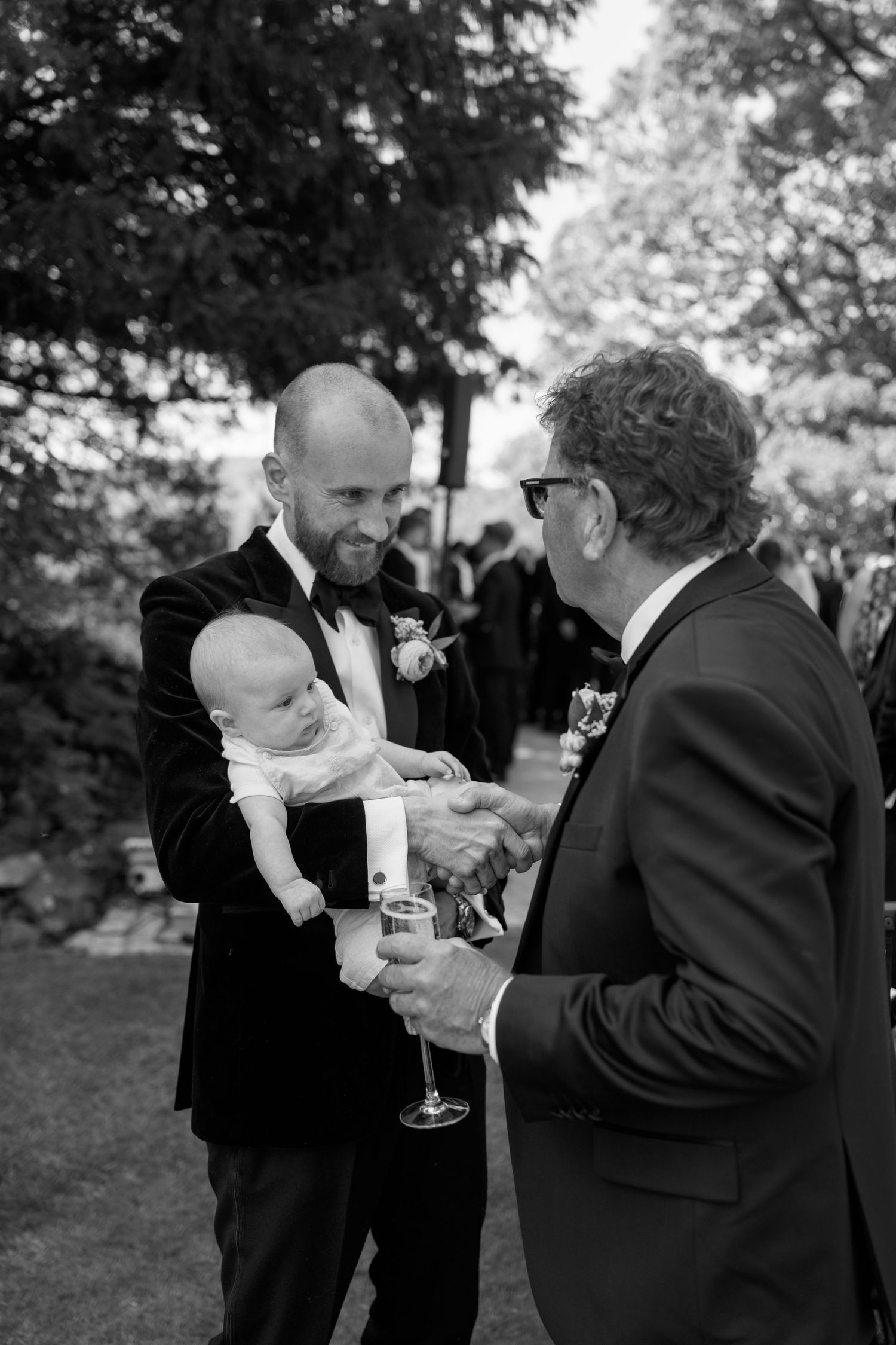 Guests in formal attire chat while holding champagne glasses at an outdoor wedding reception.