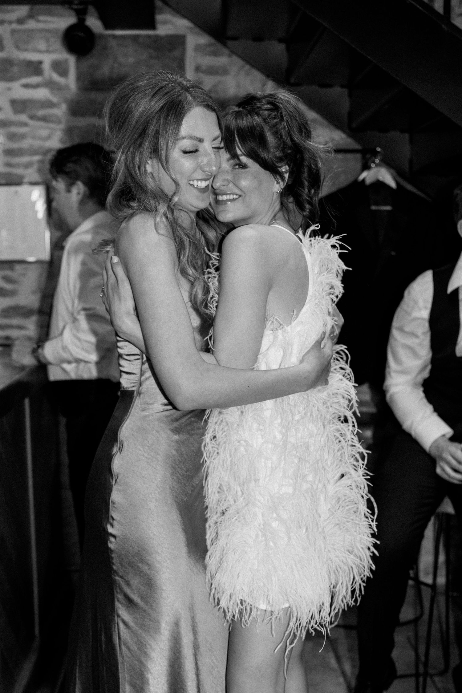 Black and white photo of two people embracing at a party in elegant dresses.