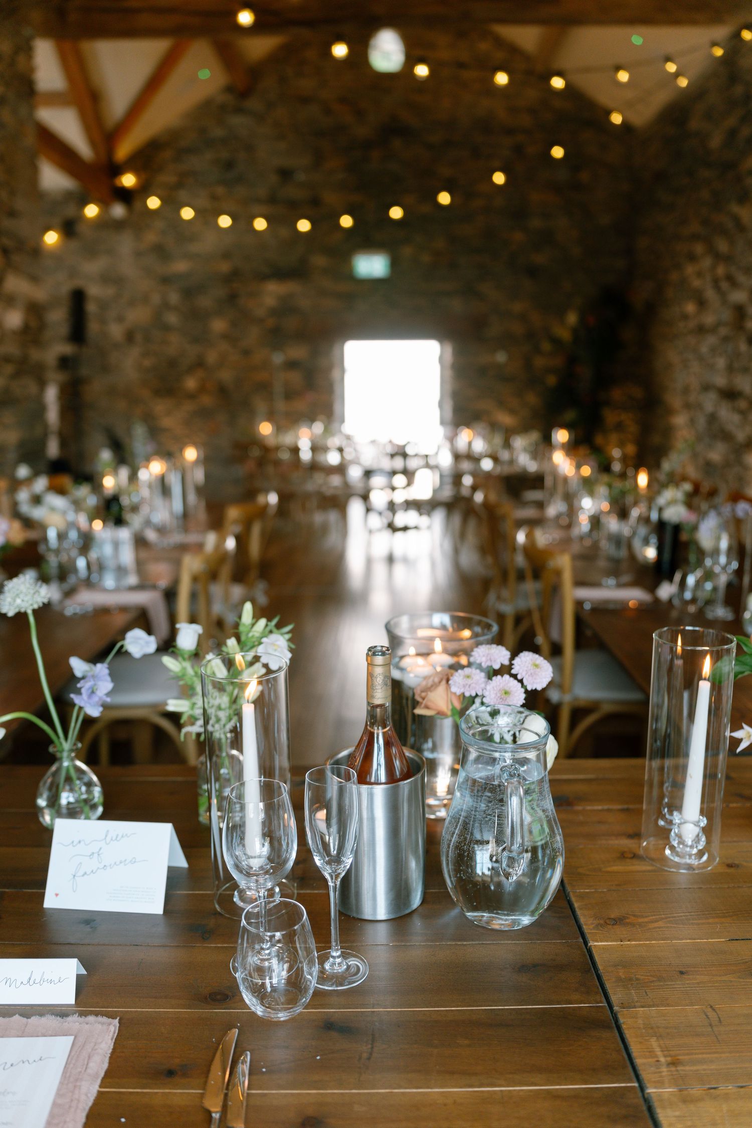 Wedding reception table settings with wine glasses and floral centerpieces in stone venue.