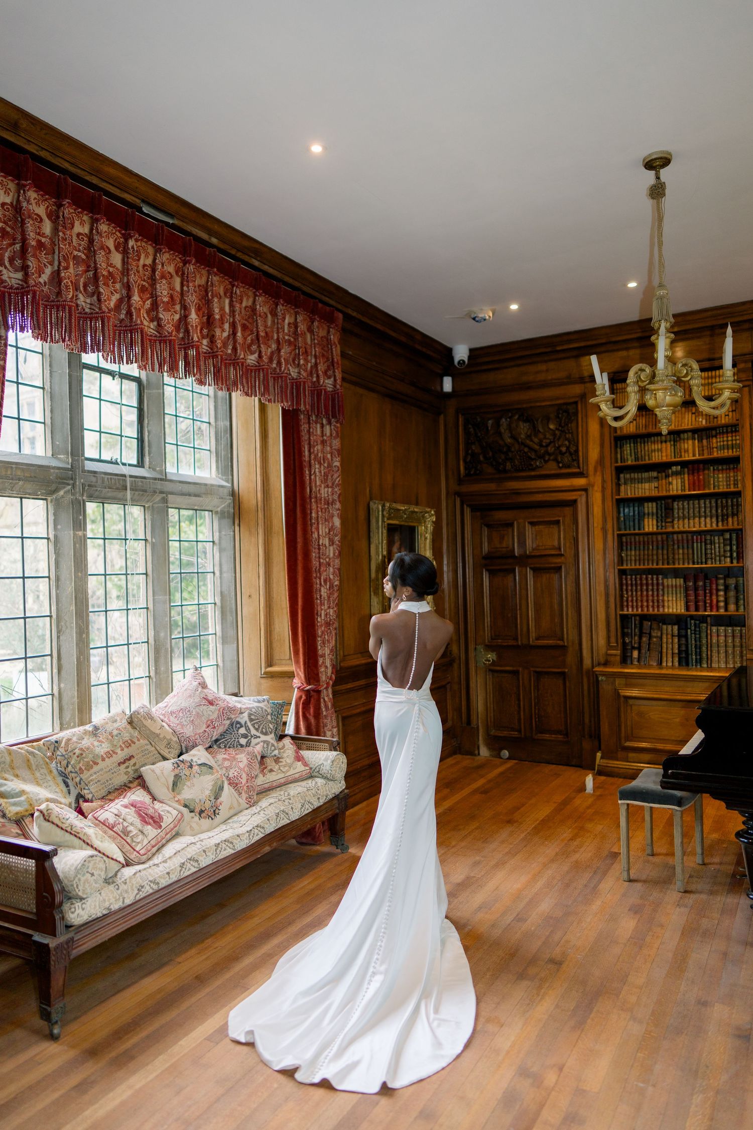 Elegant white wedding dress displayed in a wood-paneled library room with floral upholstered furniture.