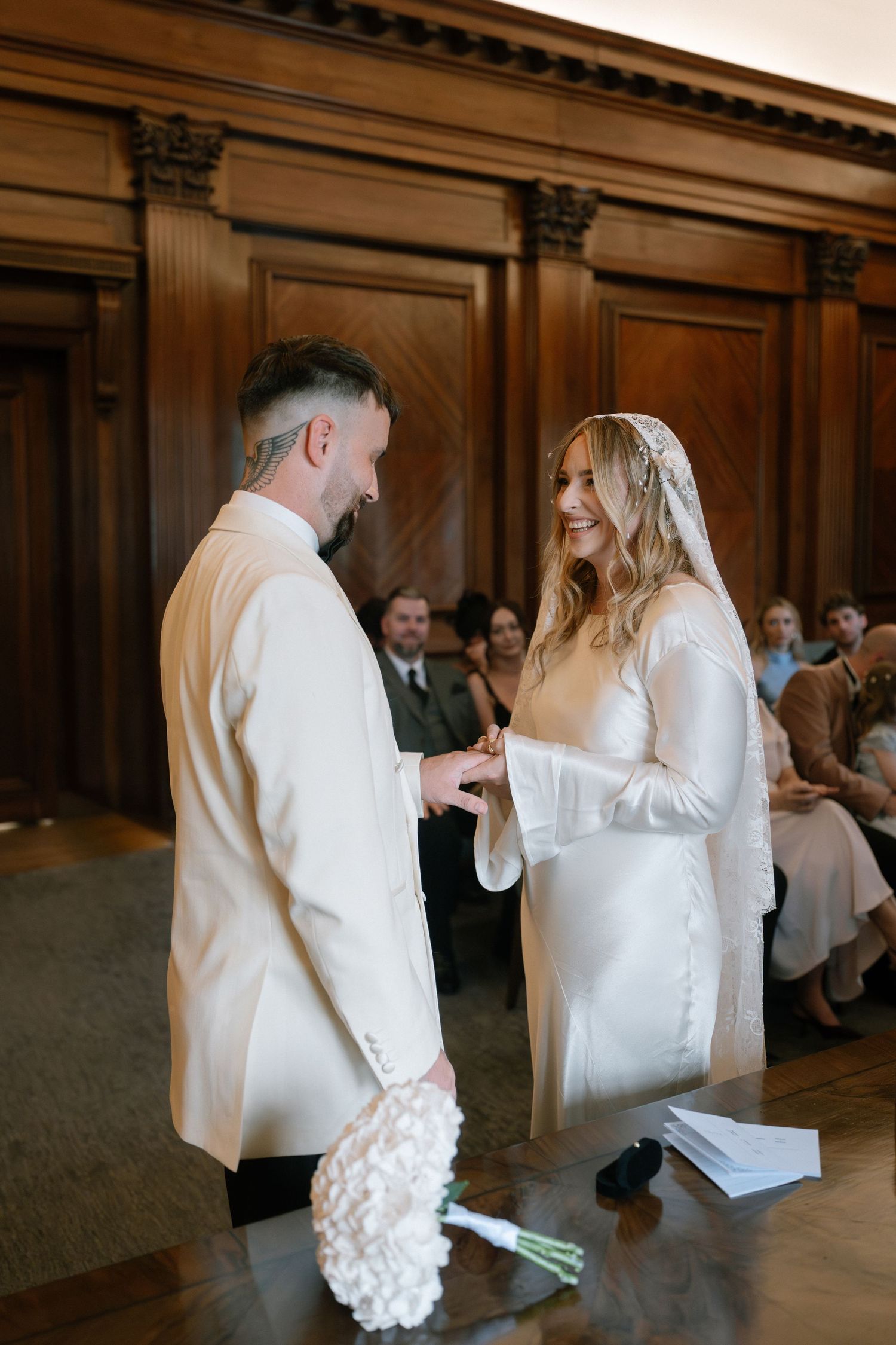 A couple exchanges rings during an intimate wedding ceremony in a wood-paneled room.