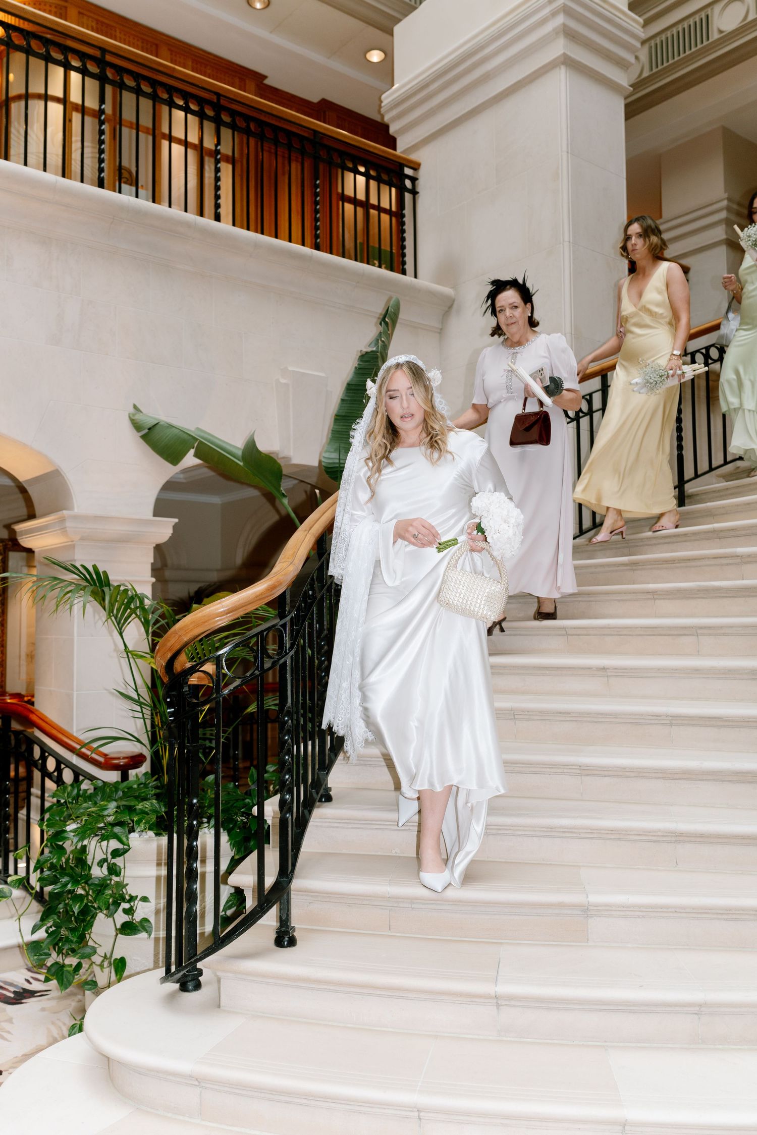 Bride and bridesmaids posing playfully on grand white marble staircase.