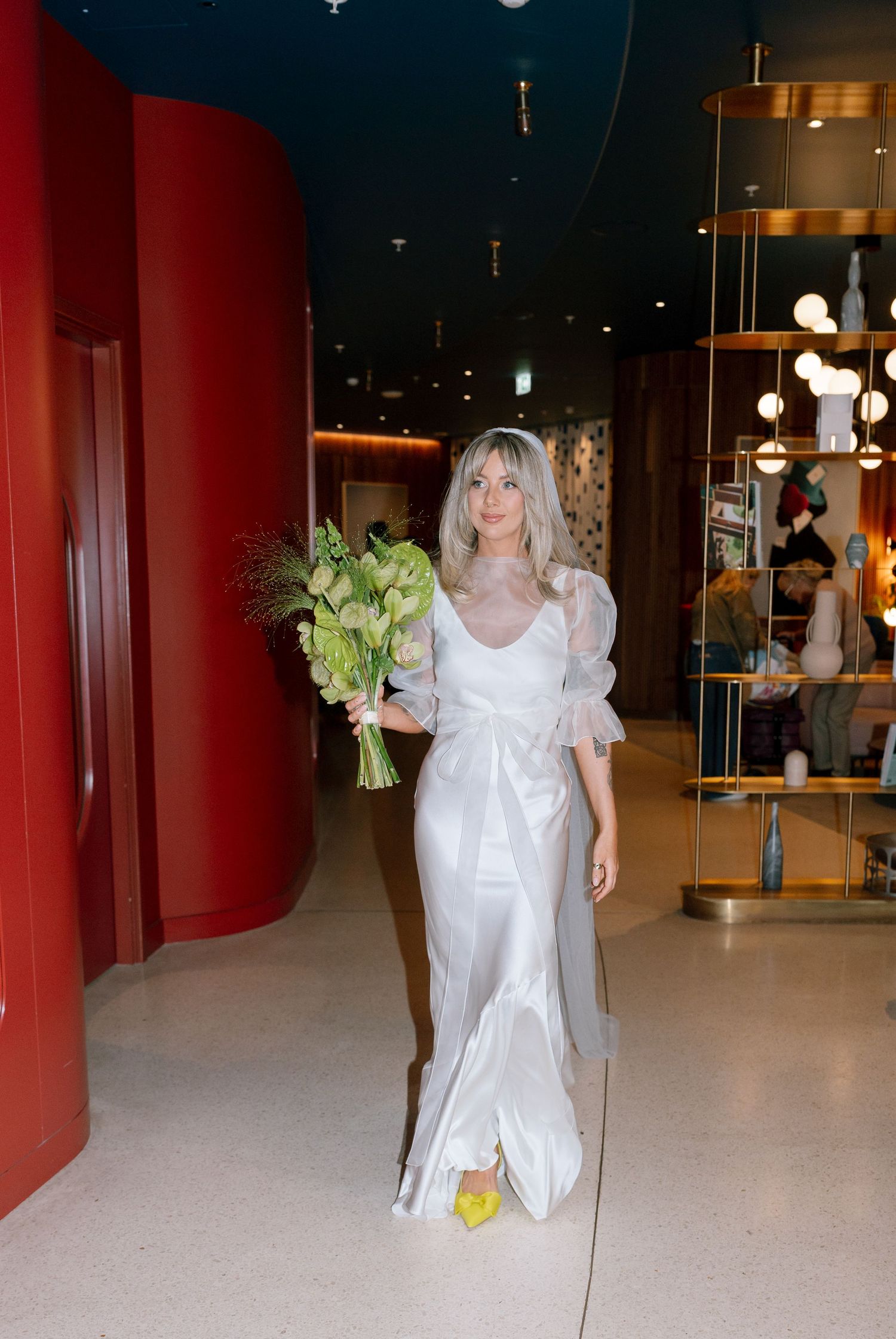 Elegant white wedding dress with puff sleeves and bouquet in modern interior with red walls.