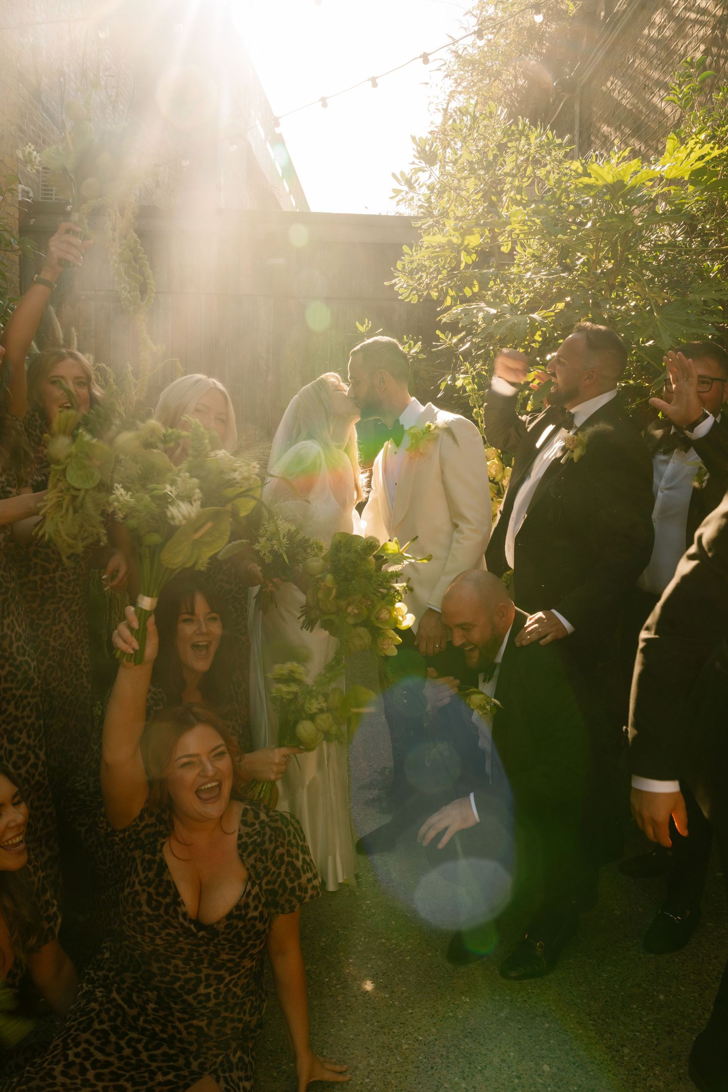 Wedding guests enjoying an outdoor celebration with sunlight streaming through trees.