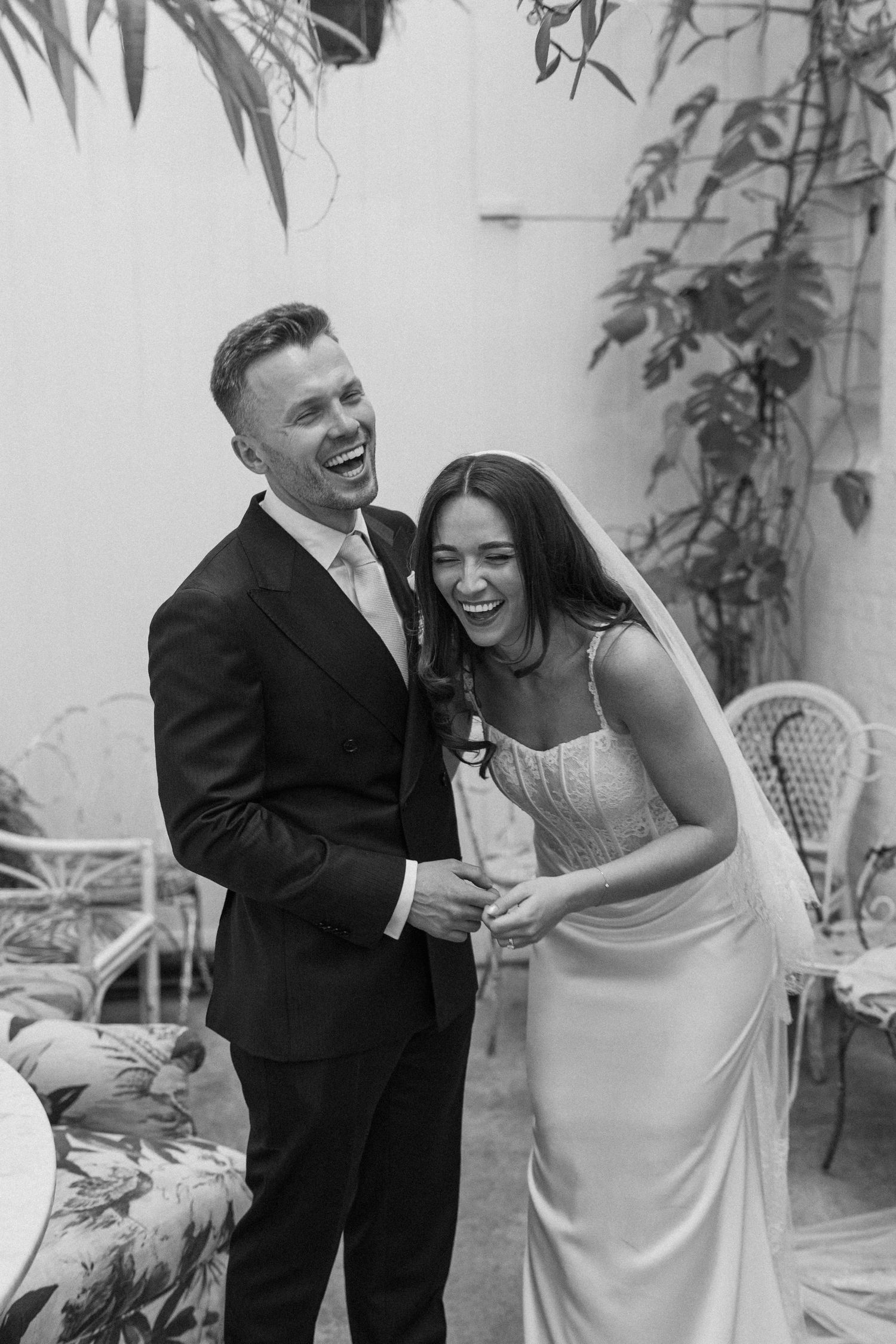 Laughing bride and groom sharing a joyful moment together in black and white wedding photo.